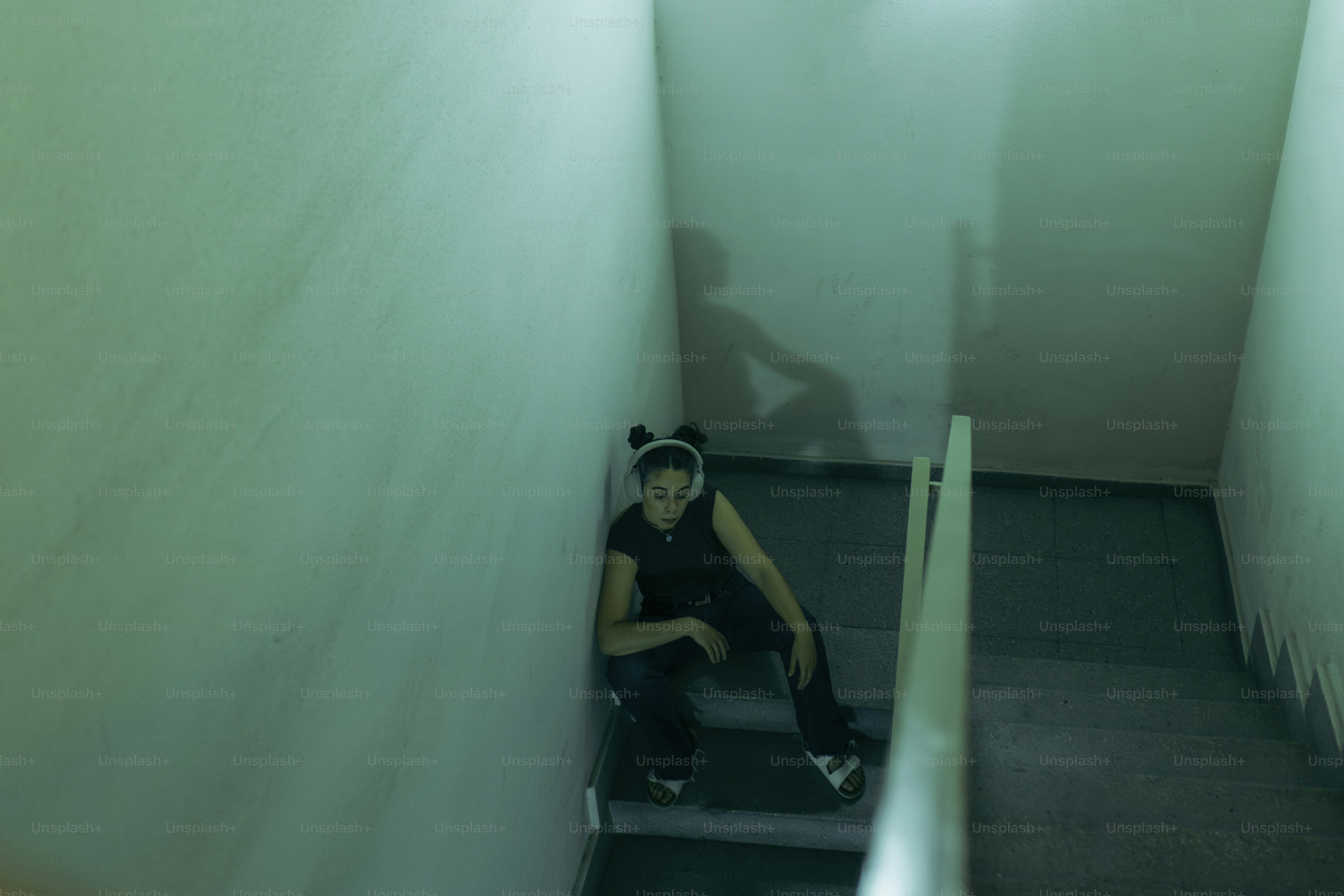 Young woman wearing headphones sitting on staircase feeling sad