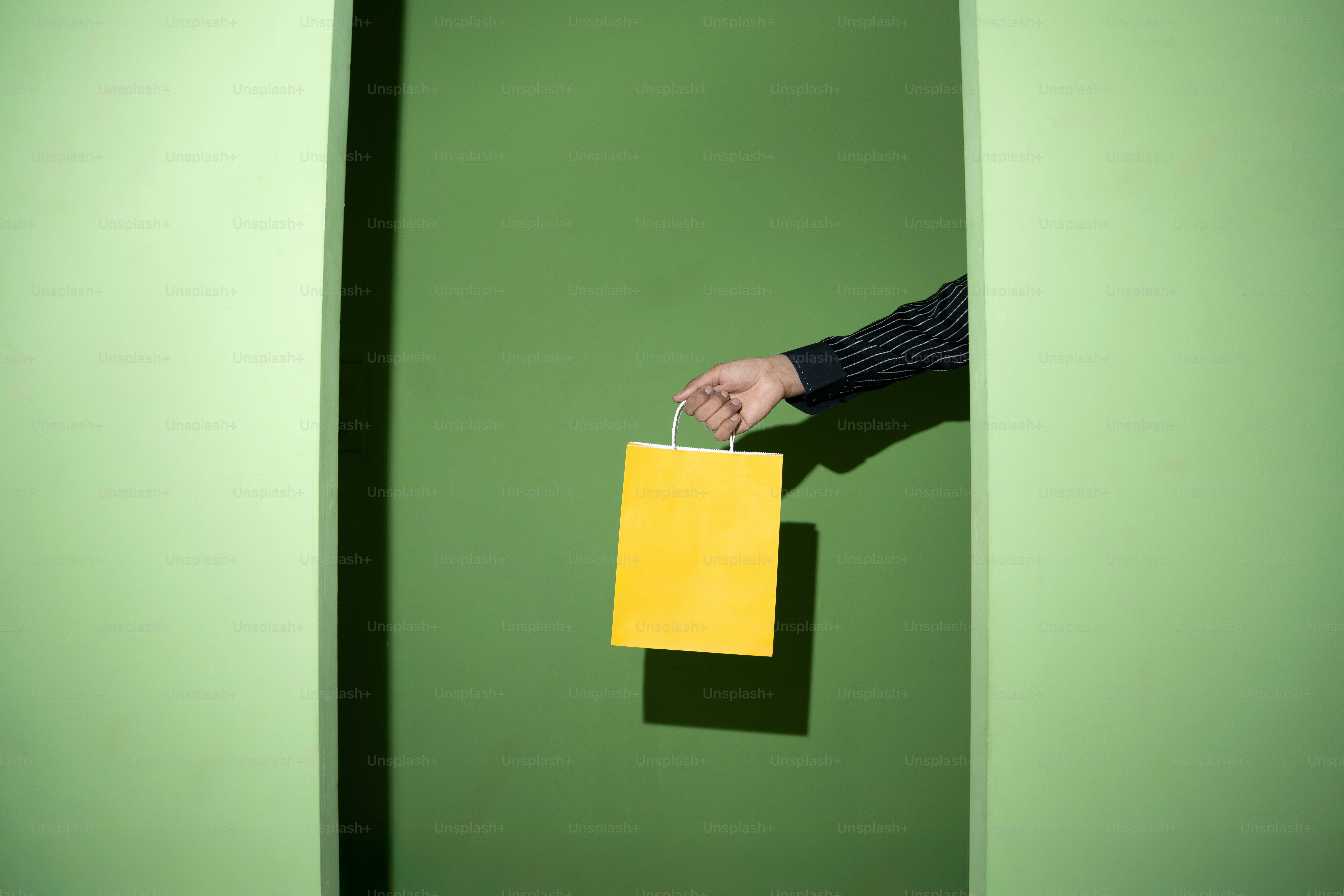 A hand offers a yellow shopping bag.