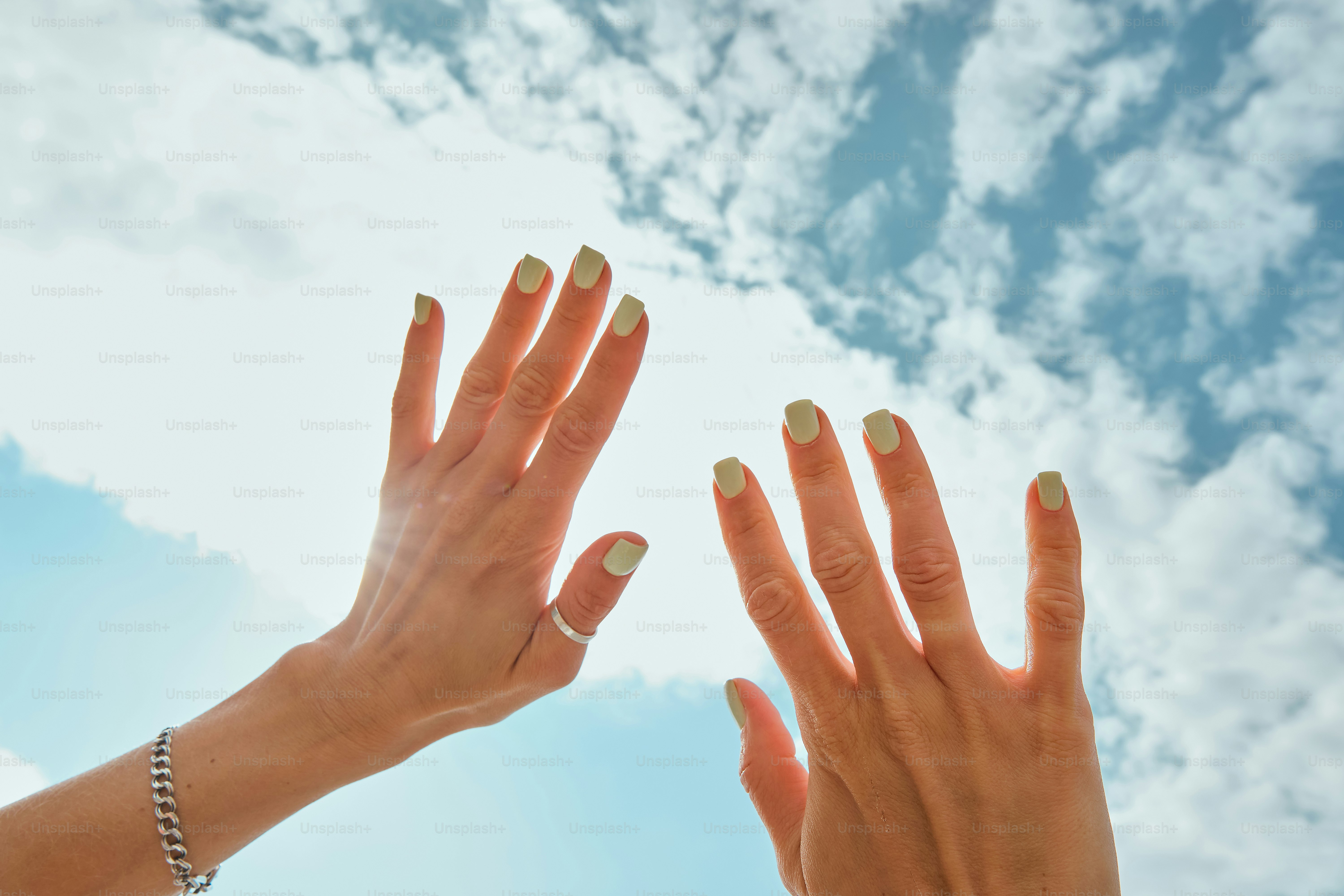 雲のある明るい青空に手が伸びる。