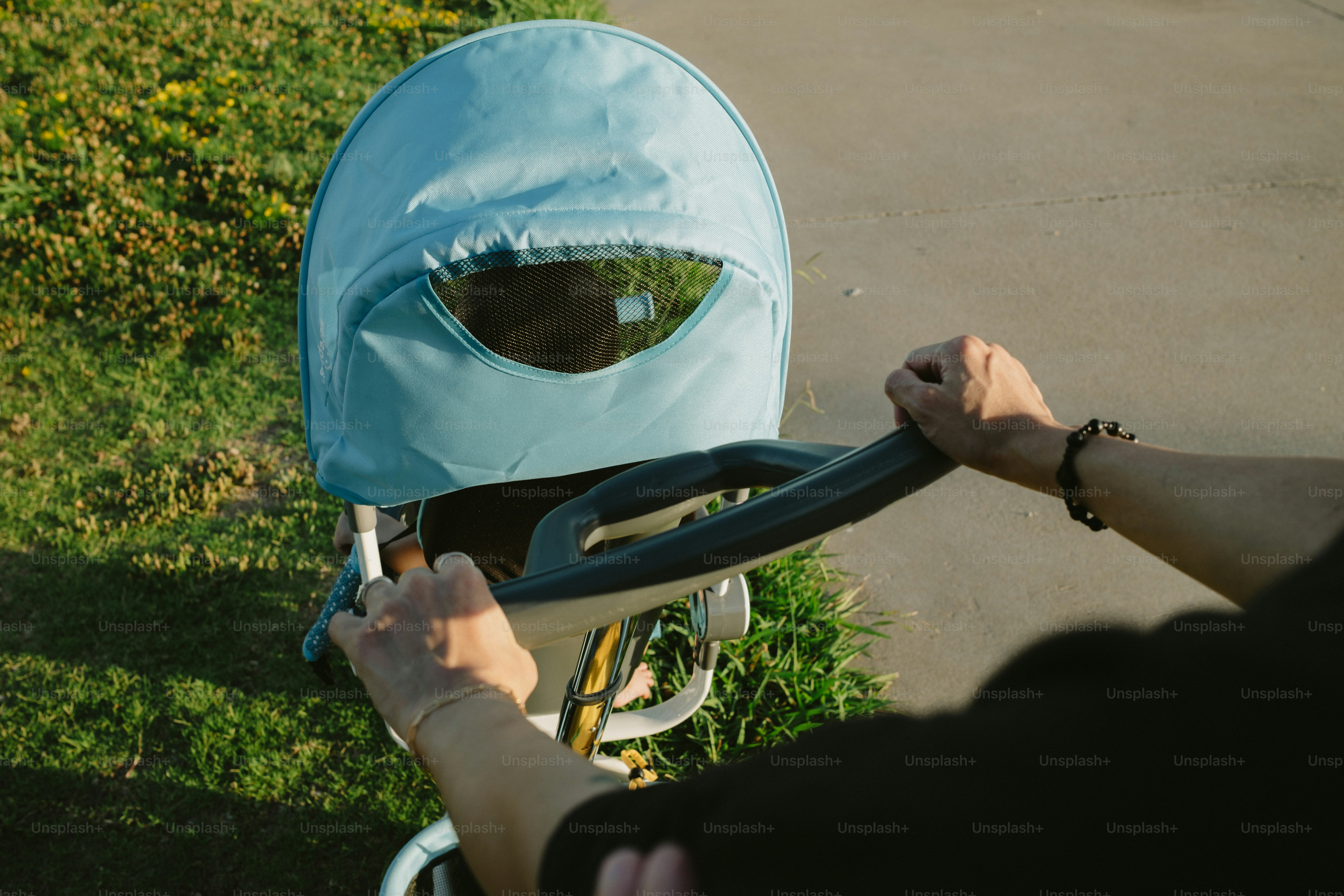 Hands push a stroller with a sun shade.