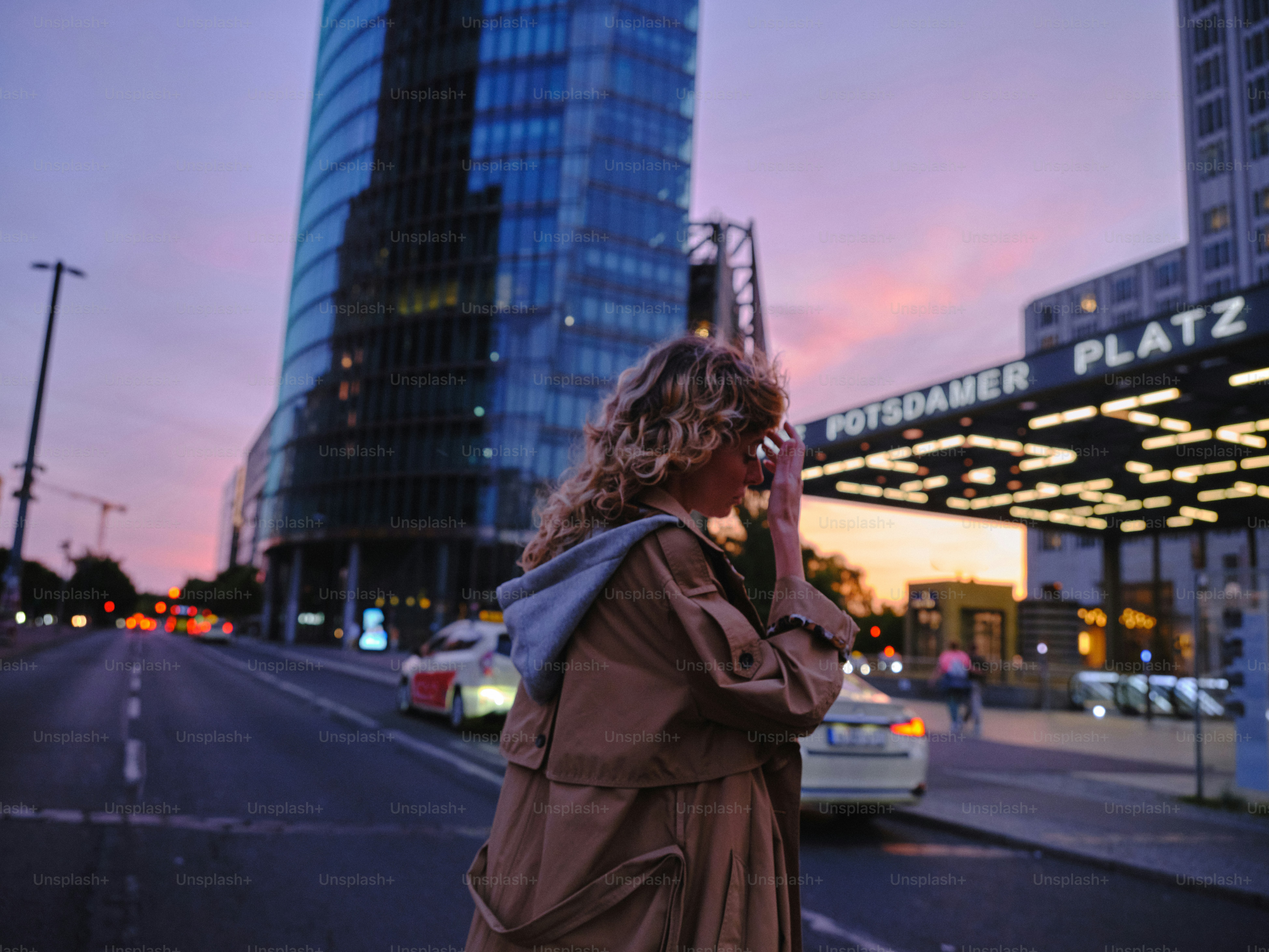 Woman walks near modern buildings at sunset.