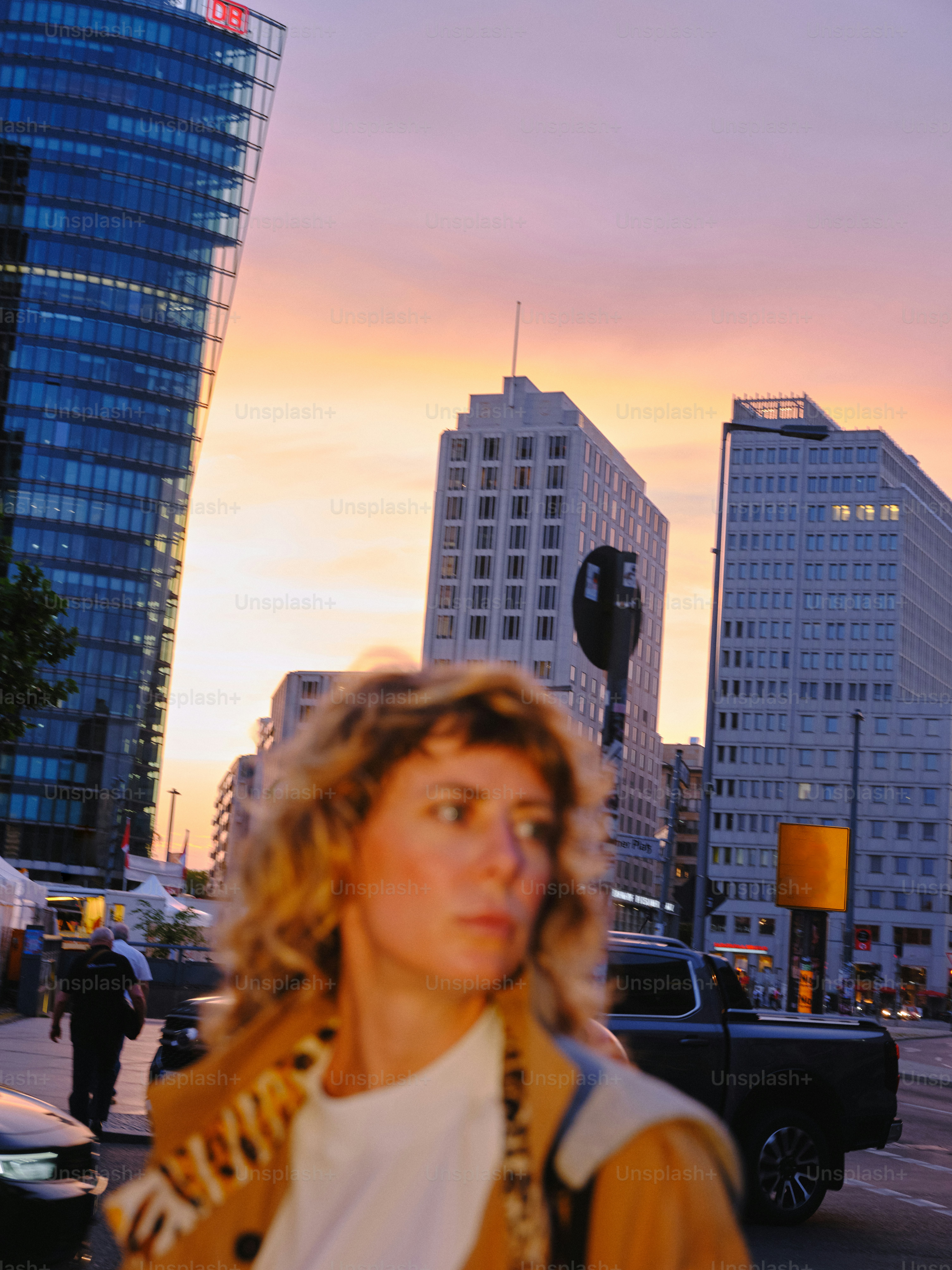 Woman stands in front of city buildings at sunset.