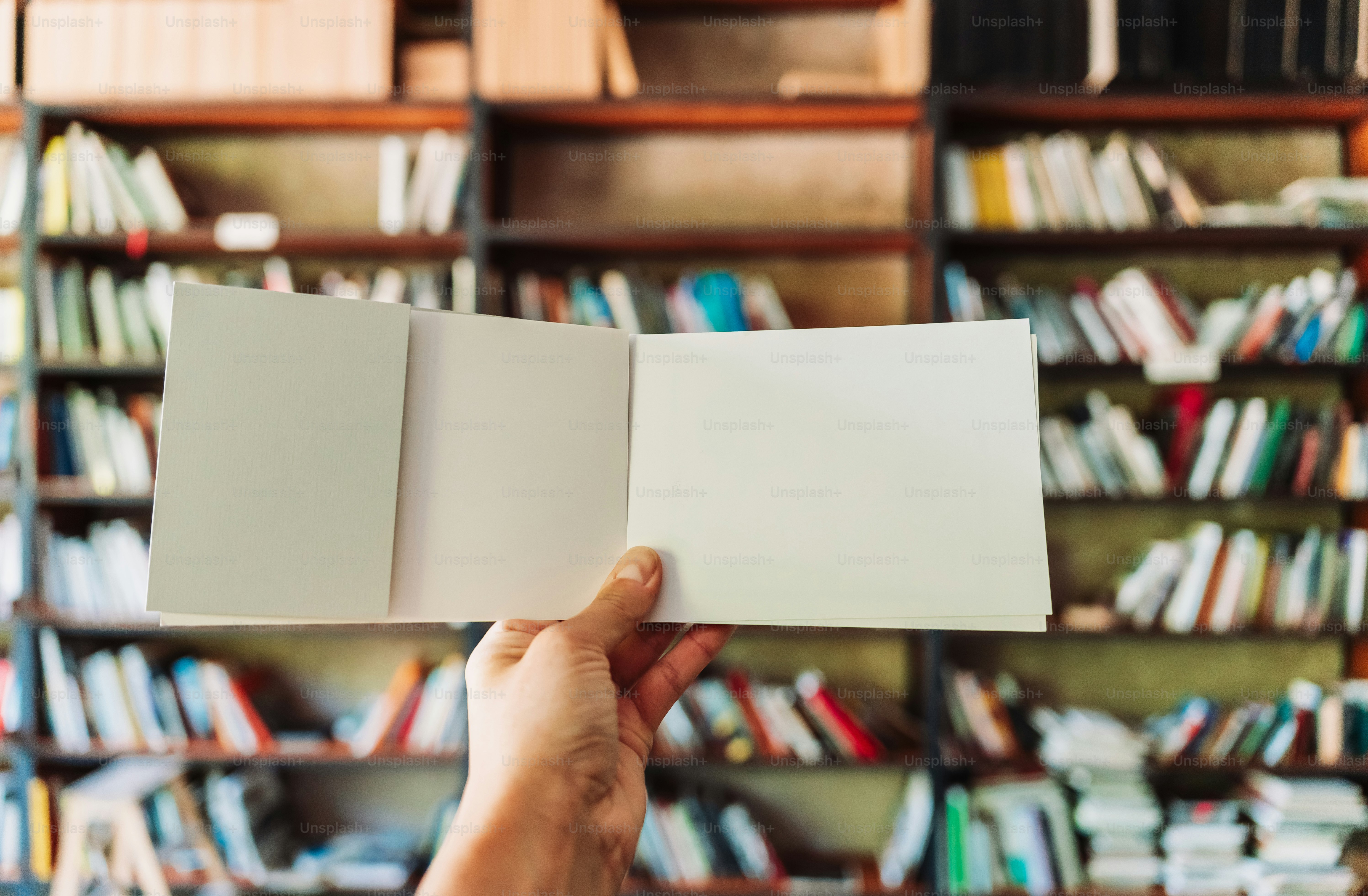 Tangan memegang buku kosong yang terbuka di perpustakaan