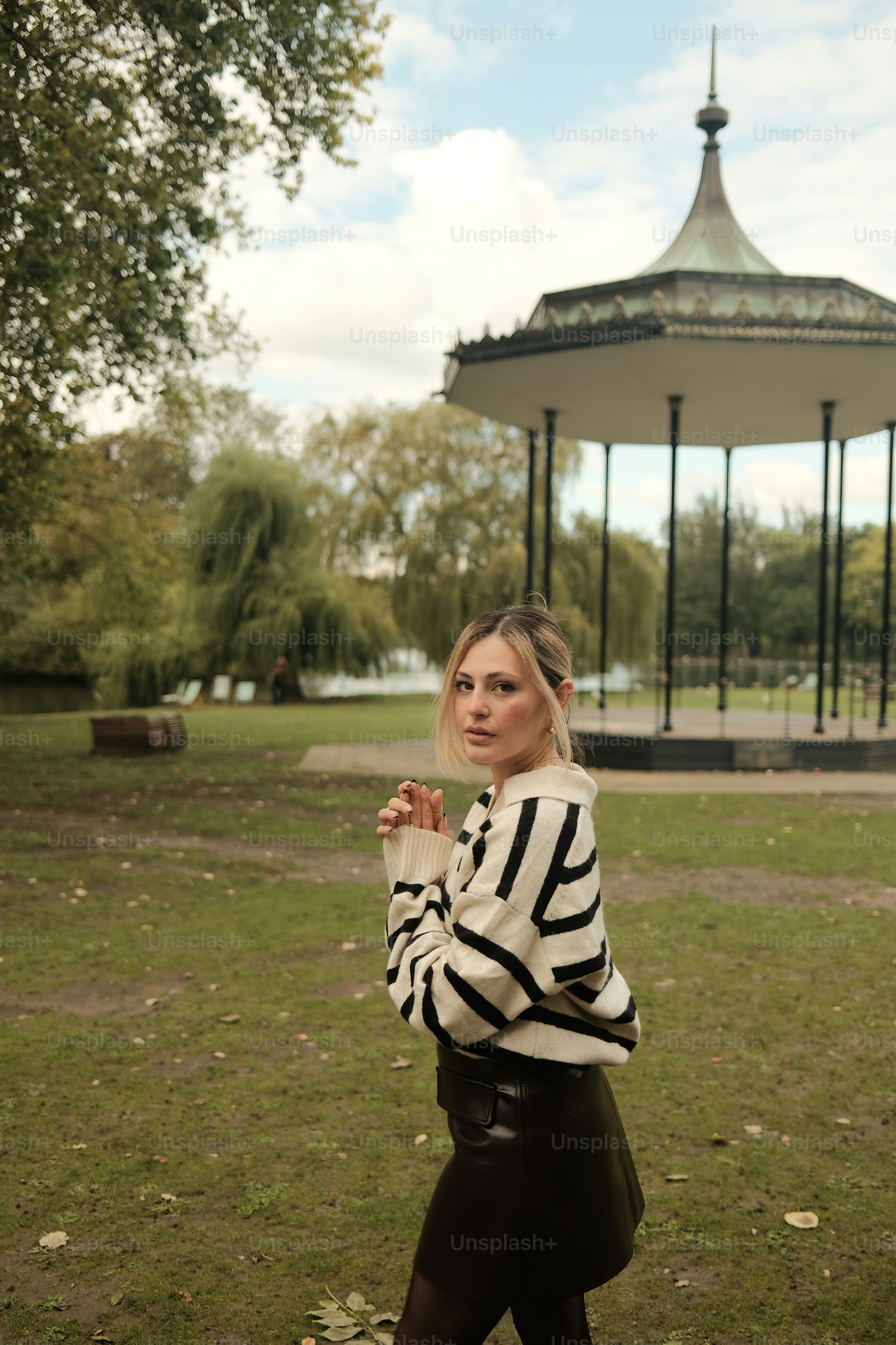 Woman poses in a park near a gazebo.