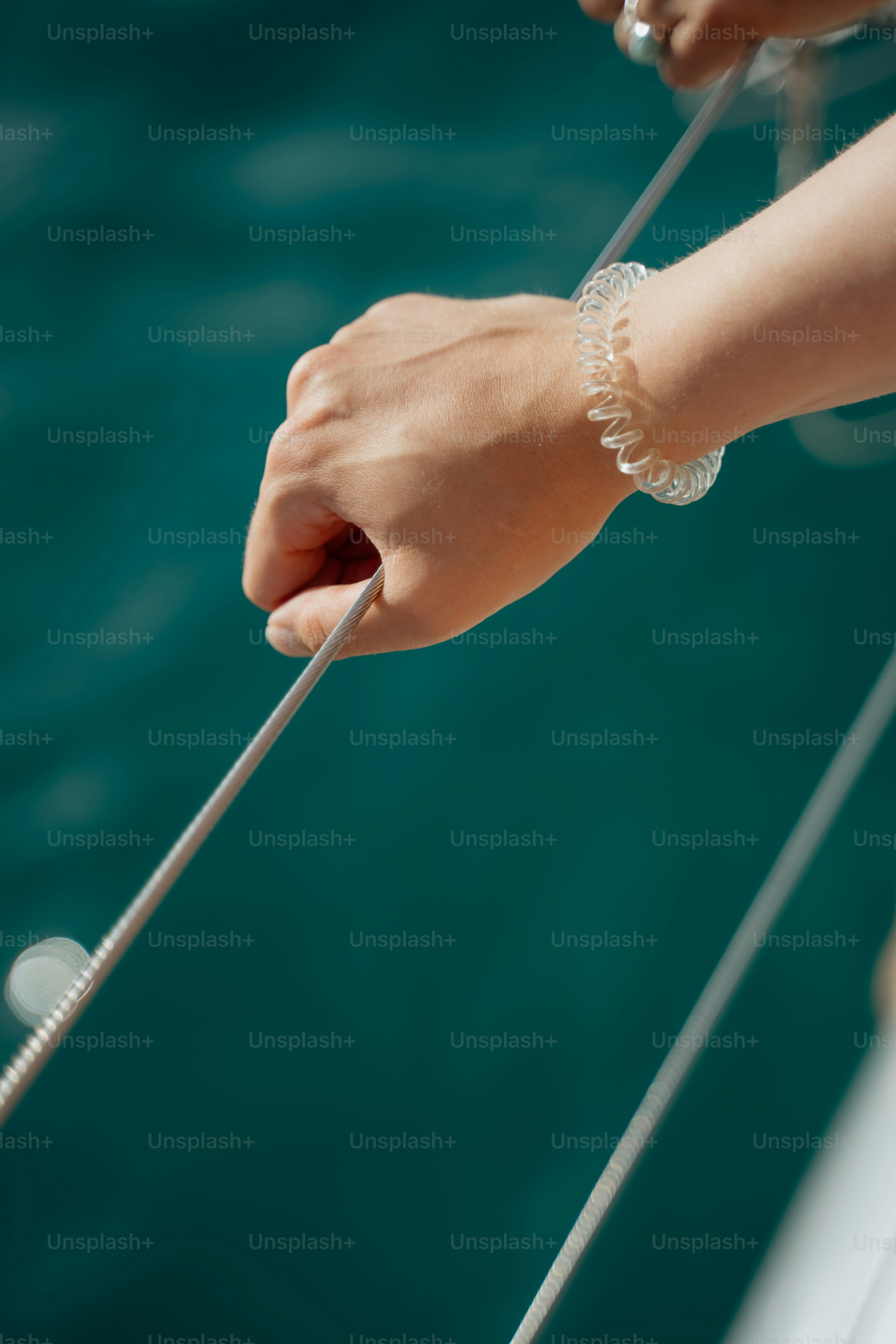 Someone's hand is holding a rope near water.