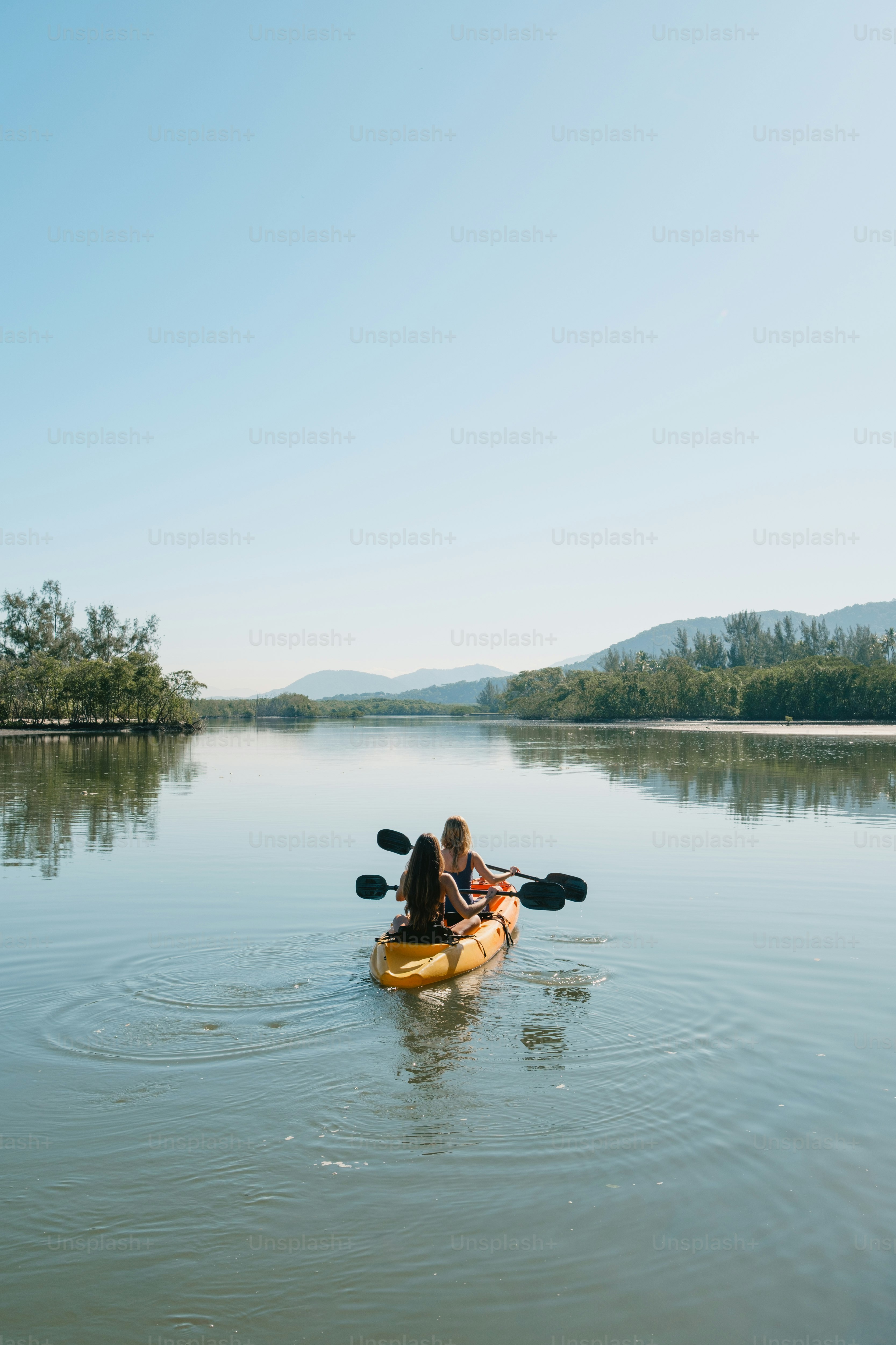 Two people kayak on a calm lake.