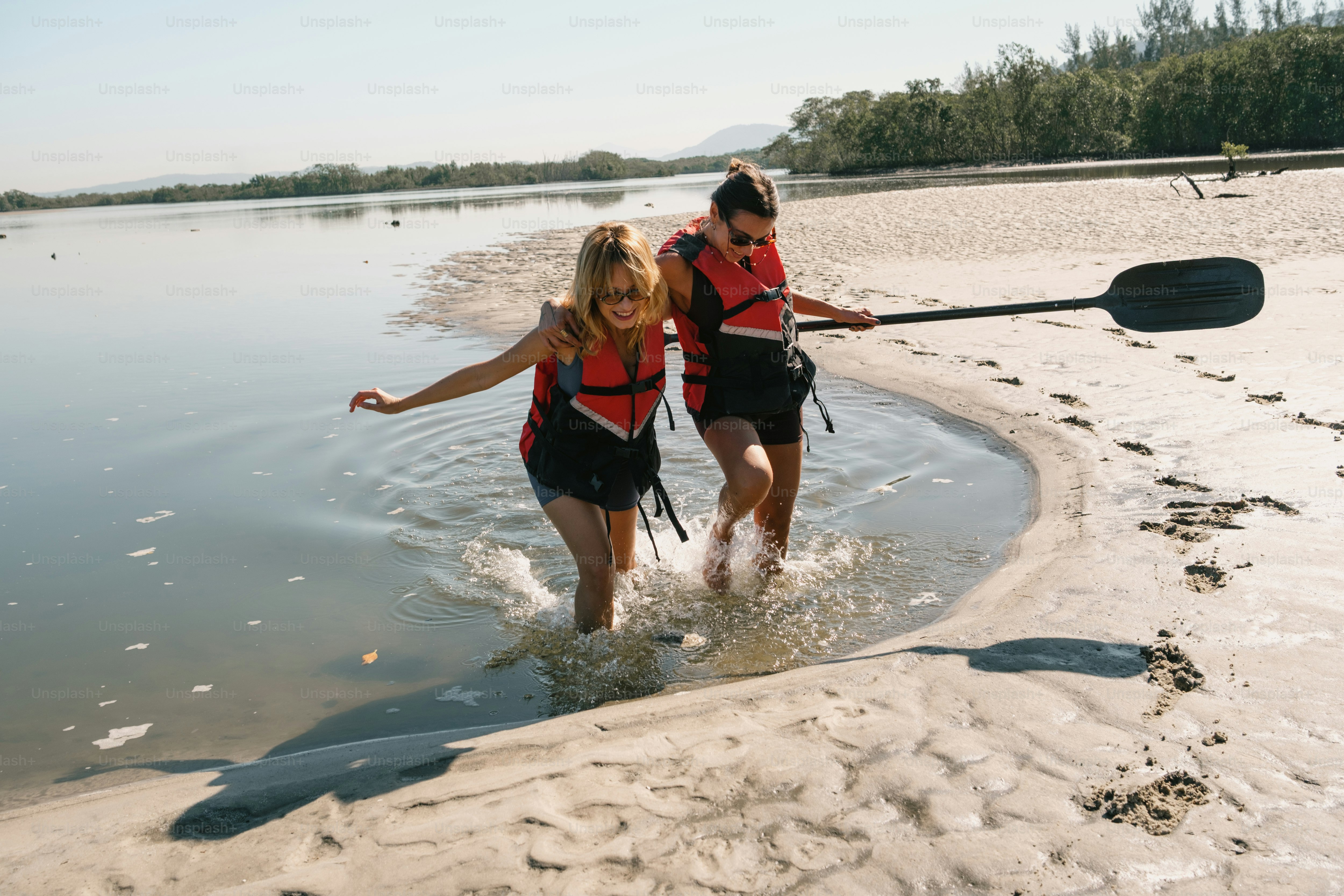 Two people walk out of the water with a paddle.