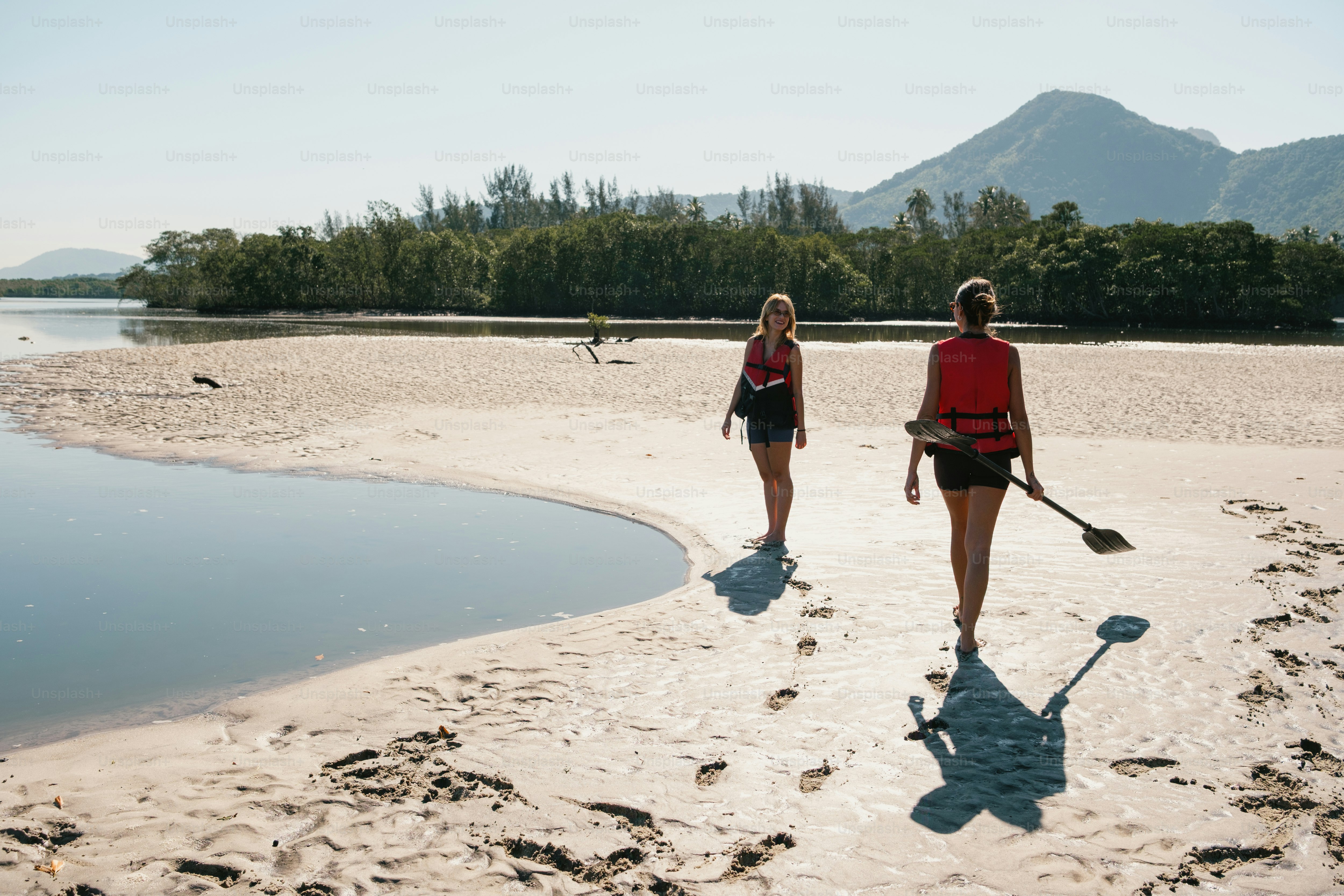 Two women walk on a beach with paddle.