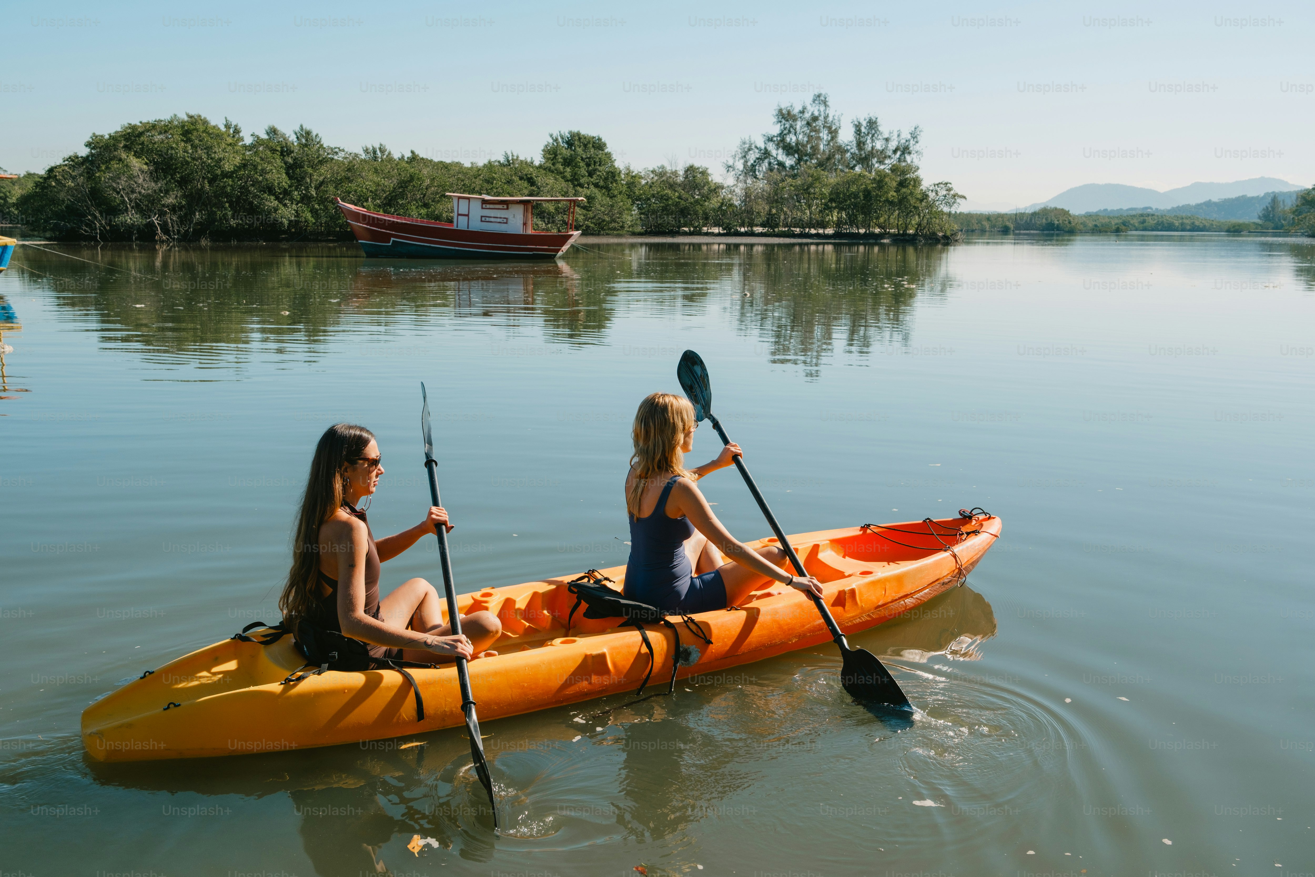 Two women kayak on a calm body of water.