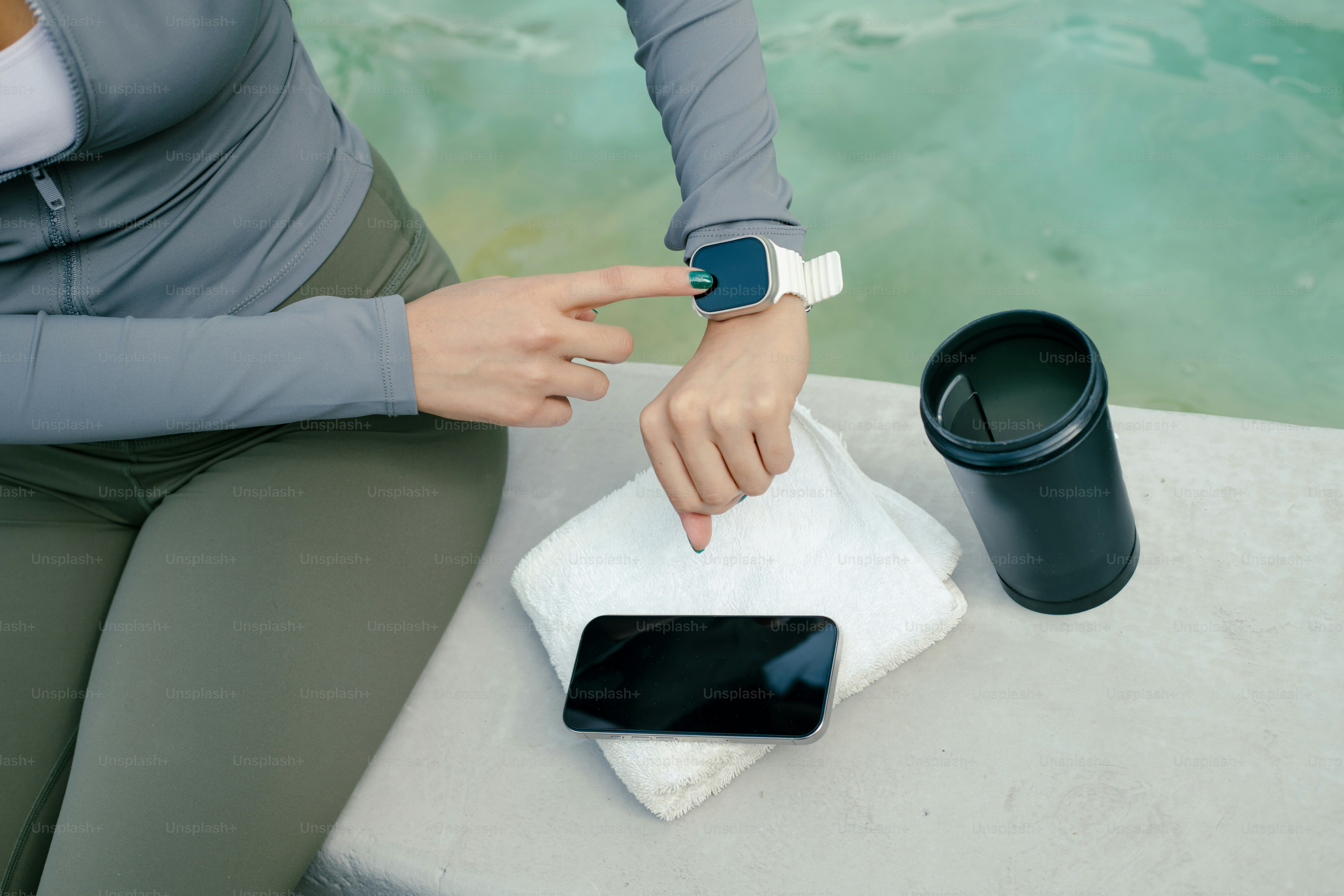 Woman checks smartwatch near pool and accessories.