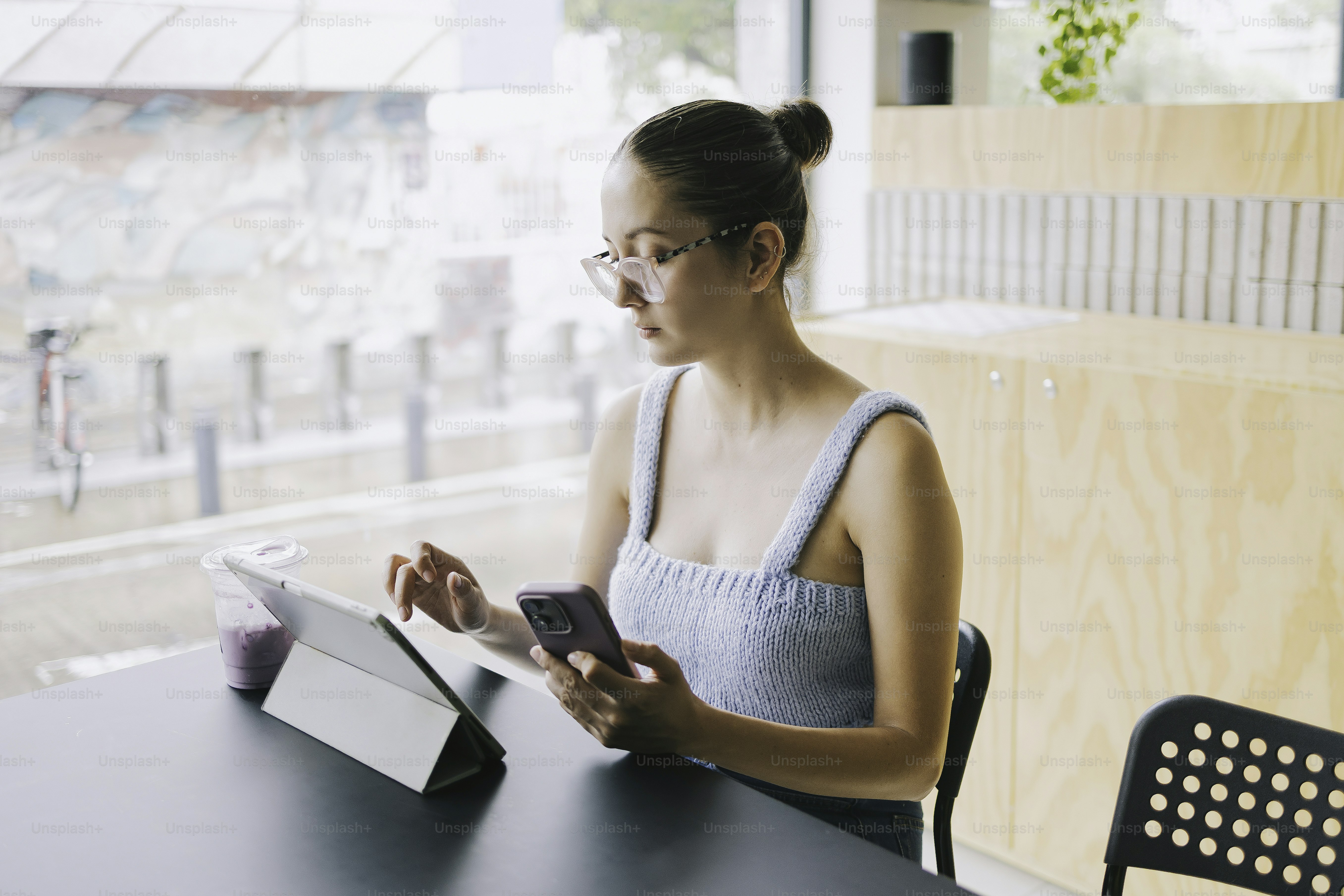 Une femme travaille sur une tablette et un téléphone à une table.