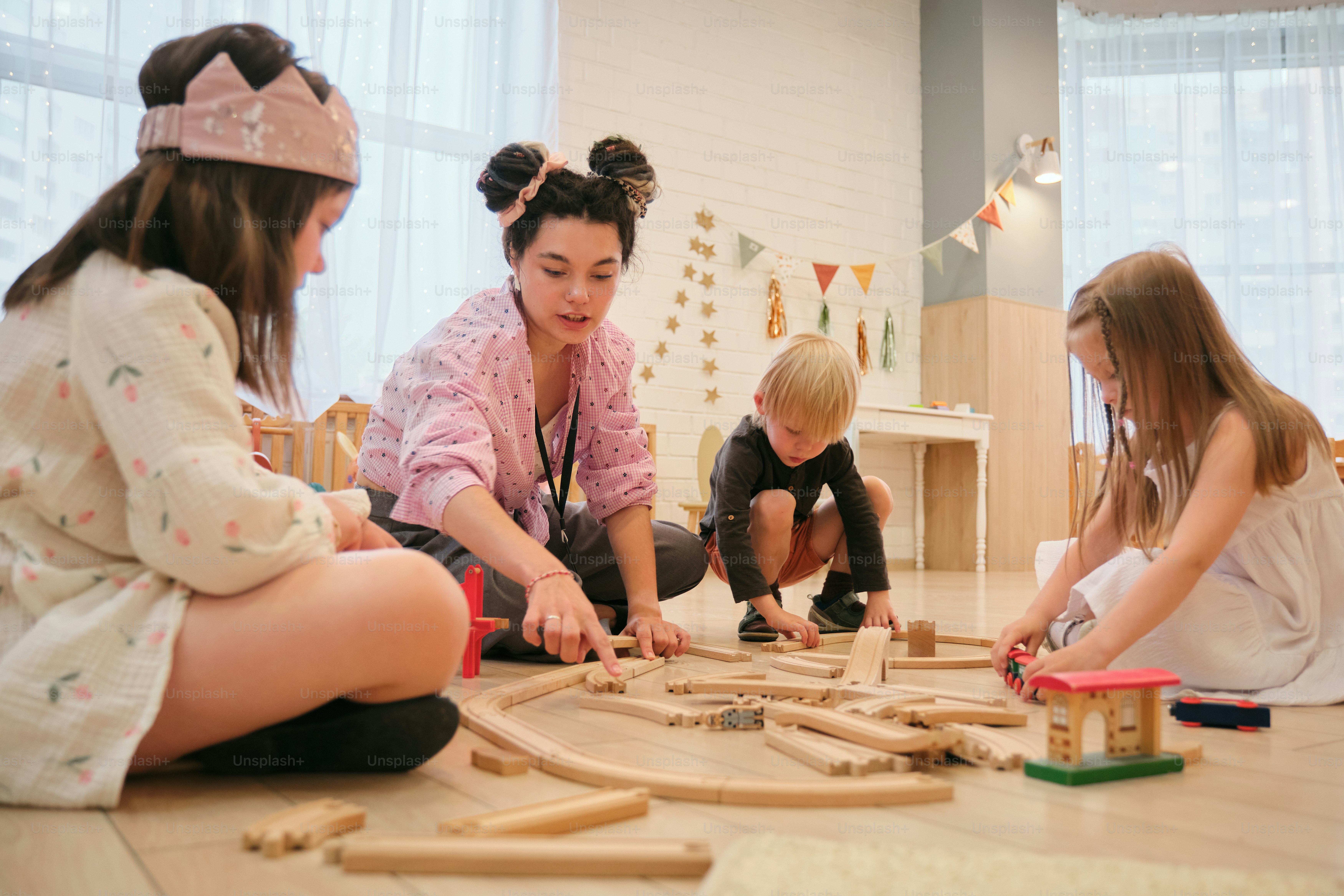Kinder und ein Lehrer spielen mit hölzernen Eisenbahnschienen.