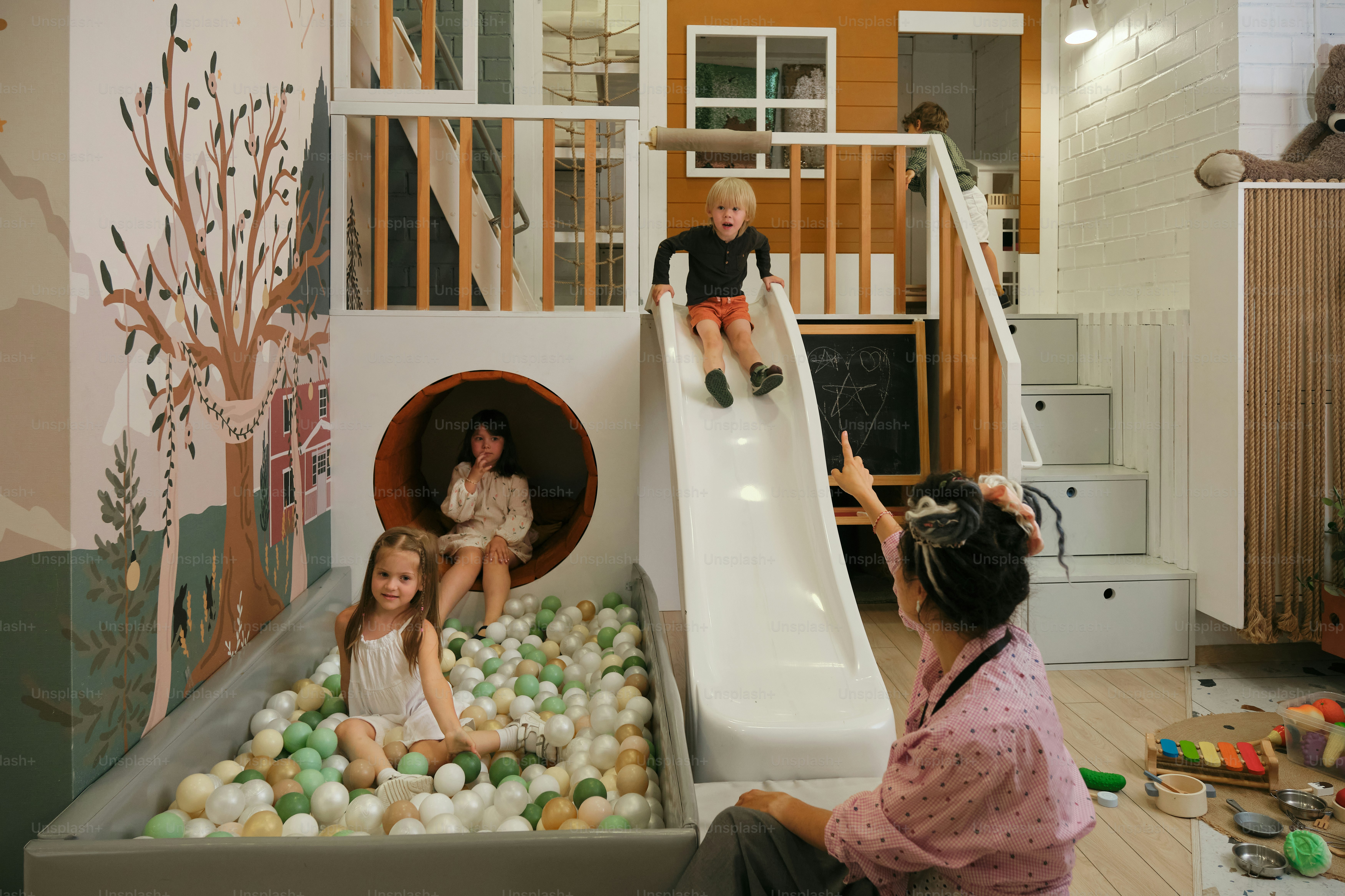 Kinder spielen auf einem bunten Indoor-Spielplatz mit Rutsche.