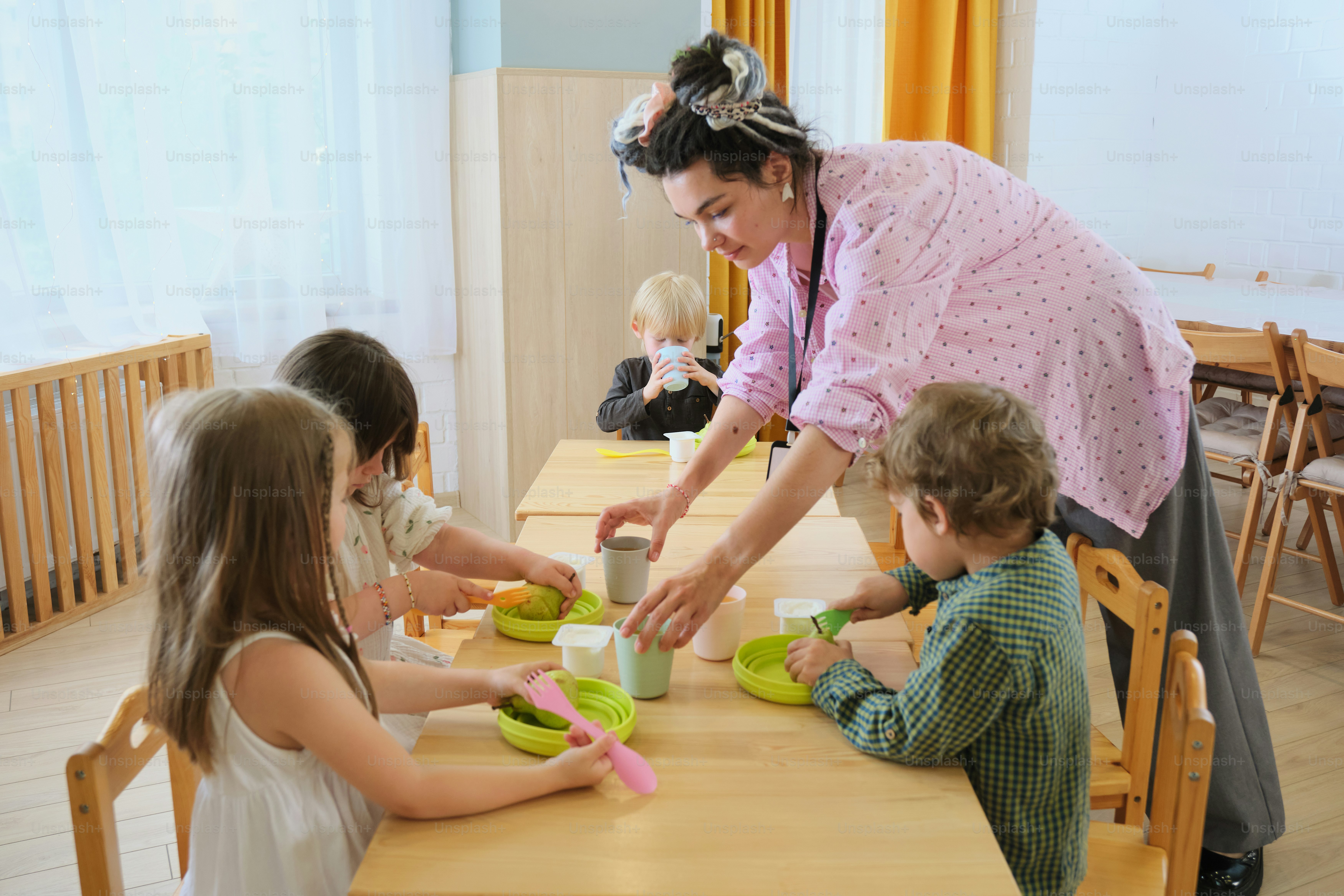 Eine Lehrerin serviert den Kindern das Mittagessen an einem Tisch.