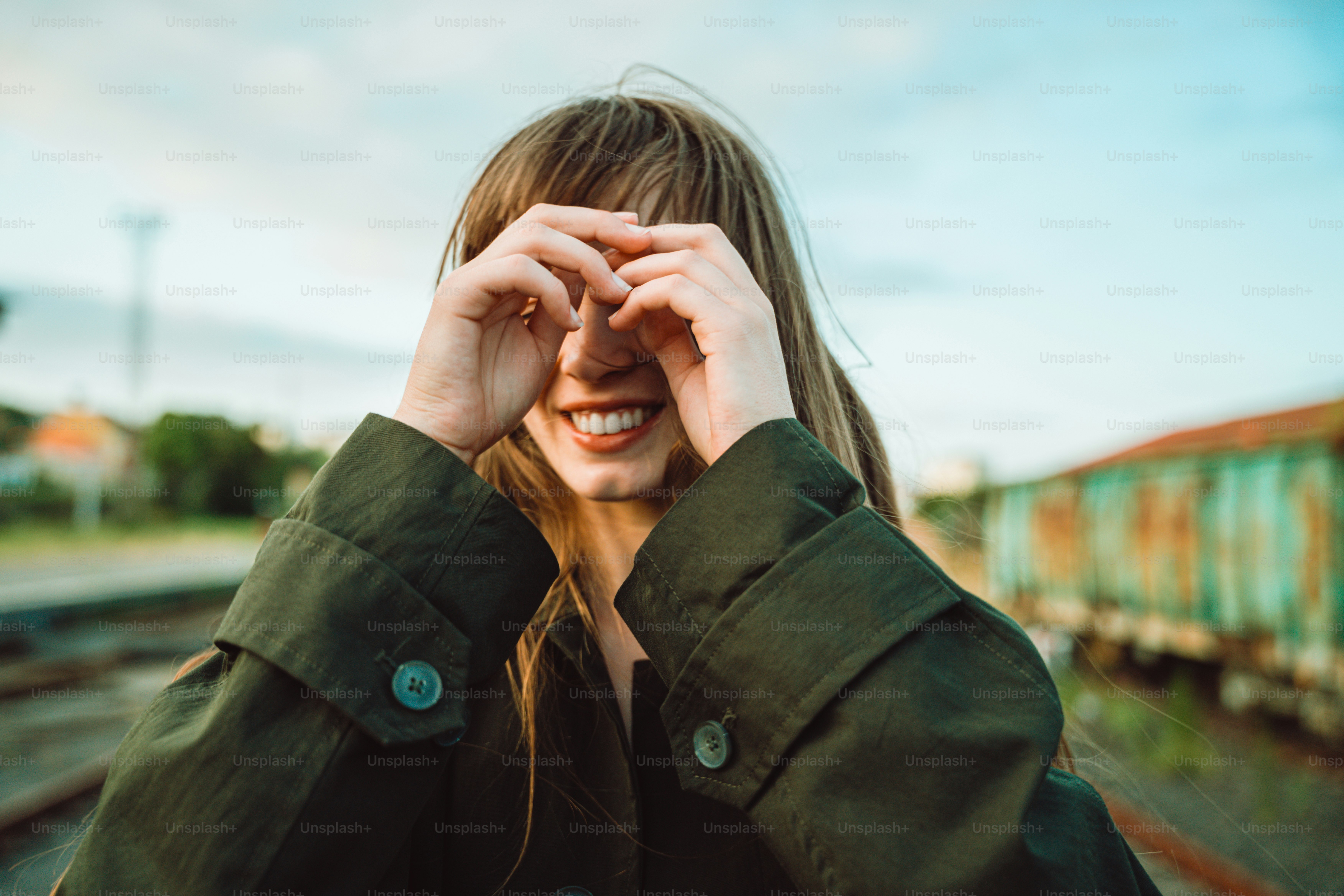 A smiling woman peers through finger-made eye holes.