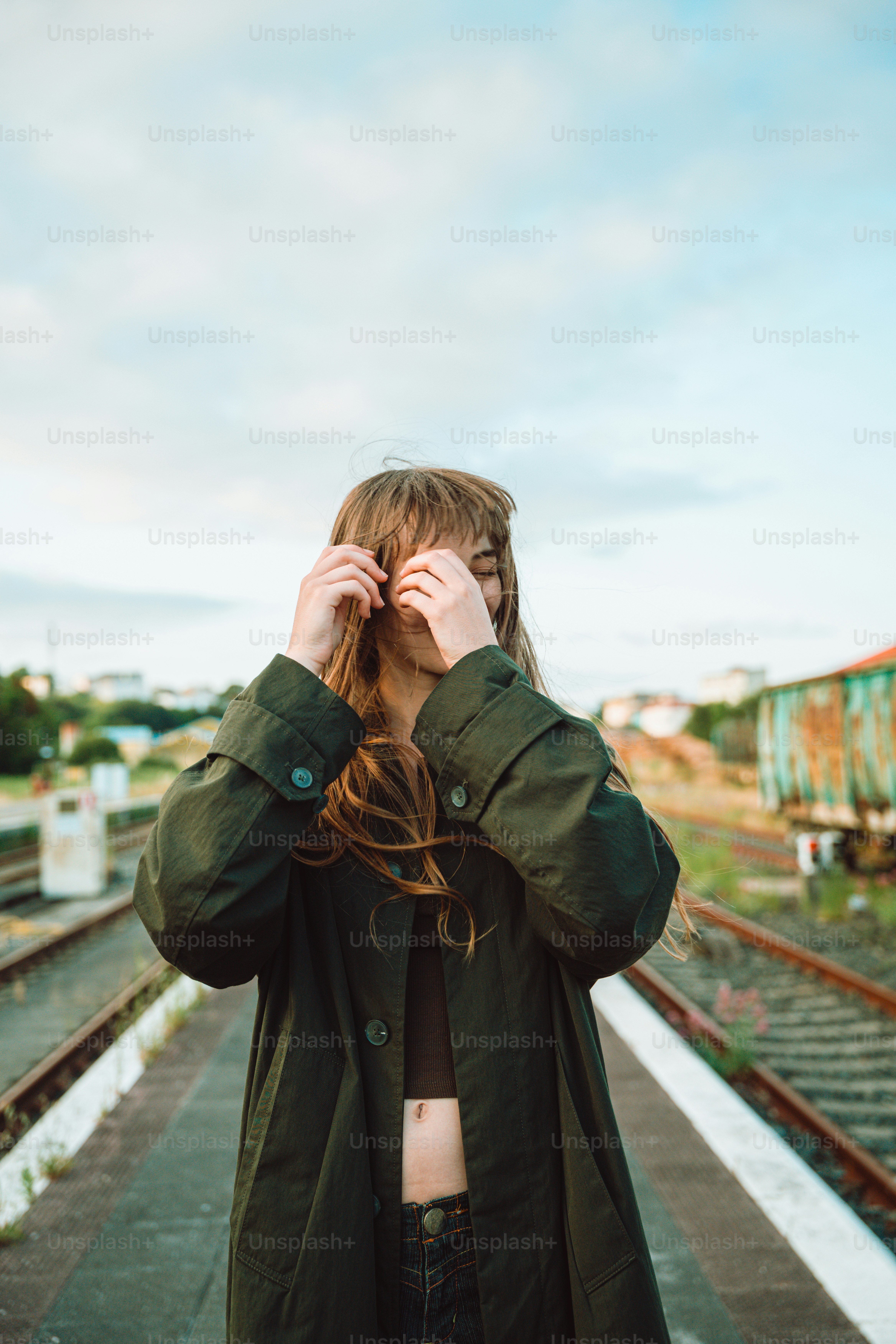 A woman stands by railroad tracks outdoors.