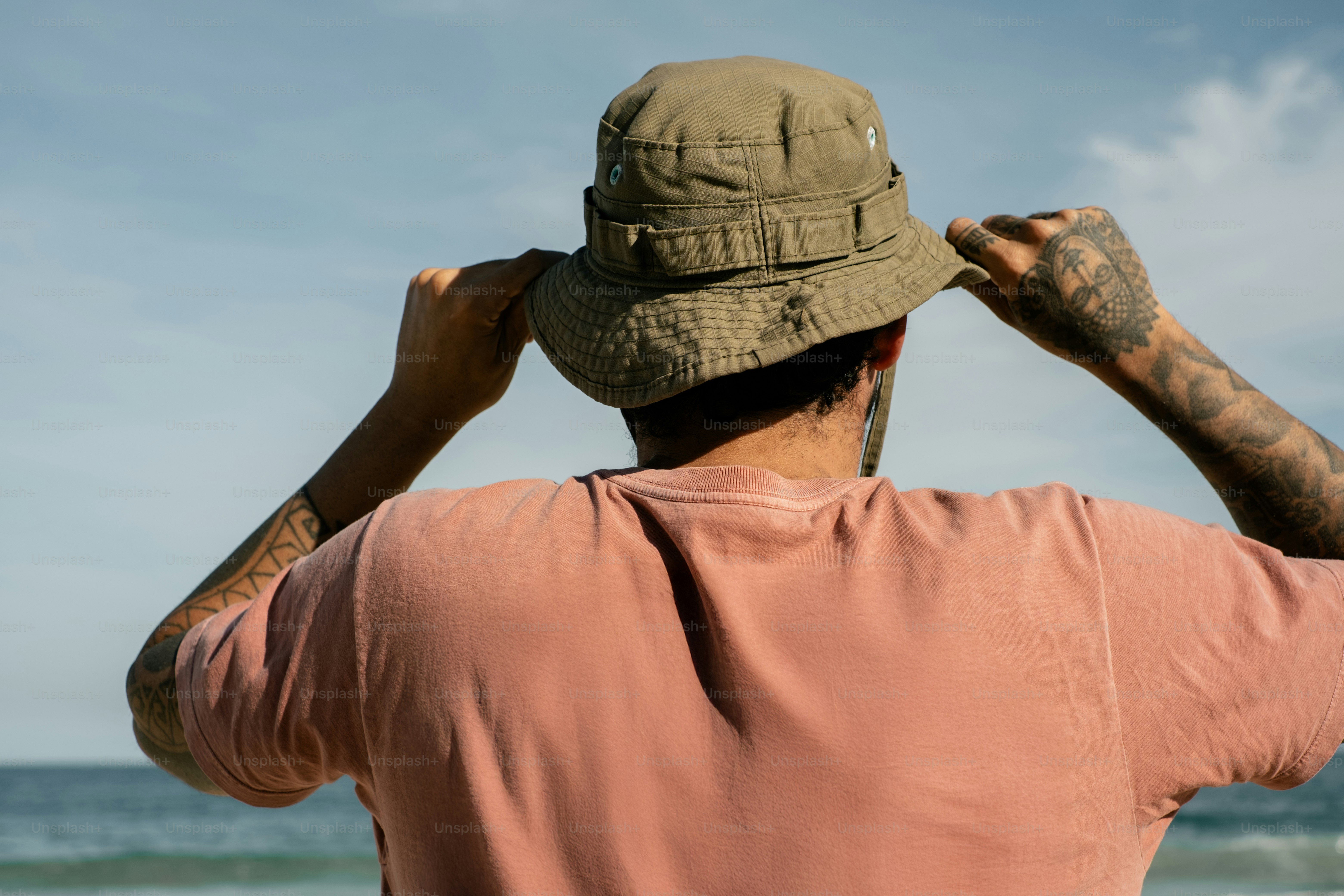 L’homme ajuste son chapeau en regardant l’océan