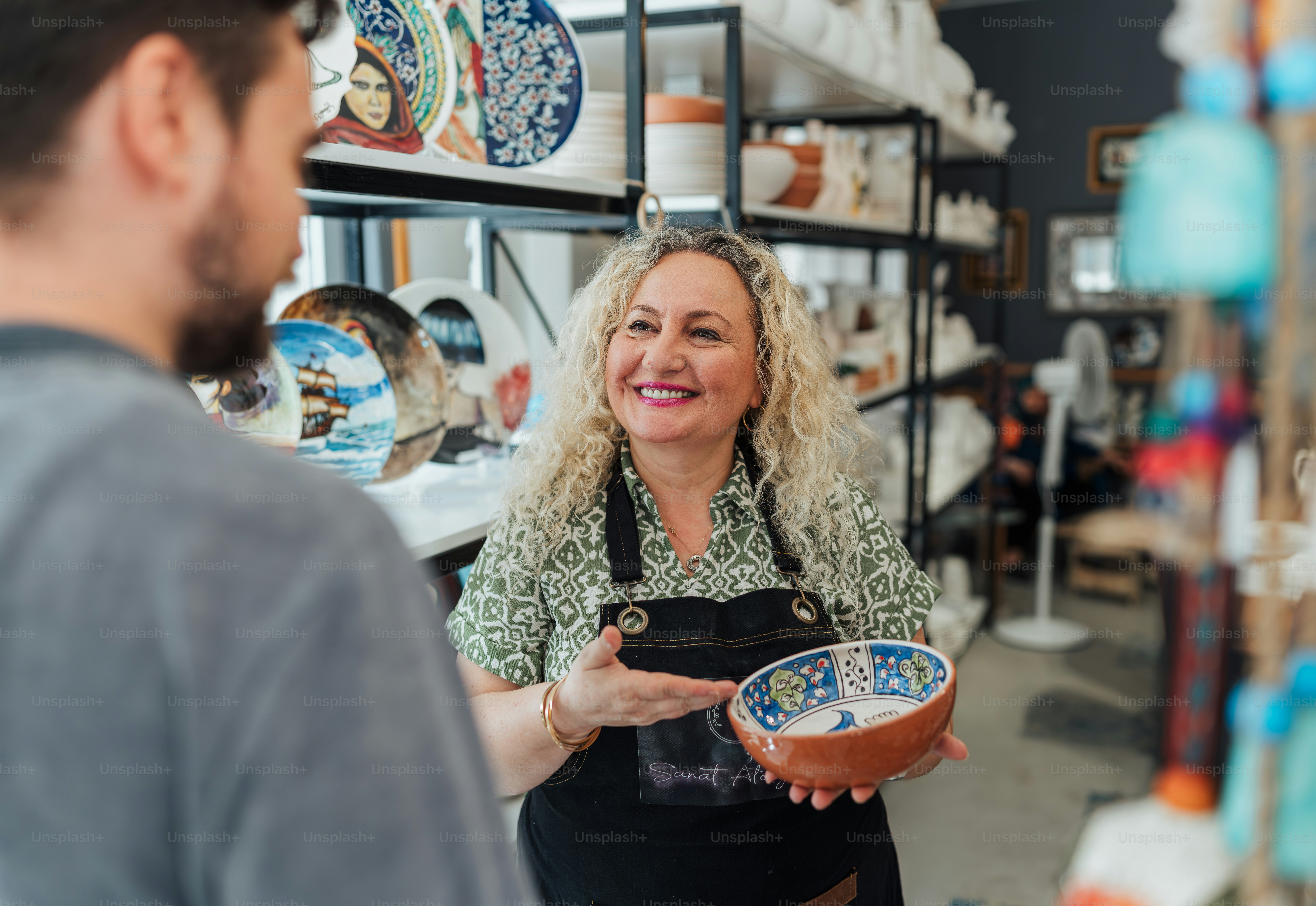 A smiling shop owner shows a bowl to a customer.
