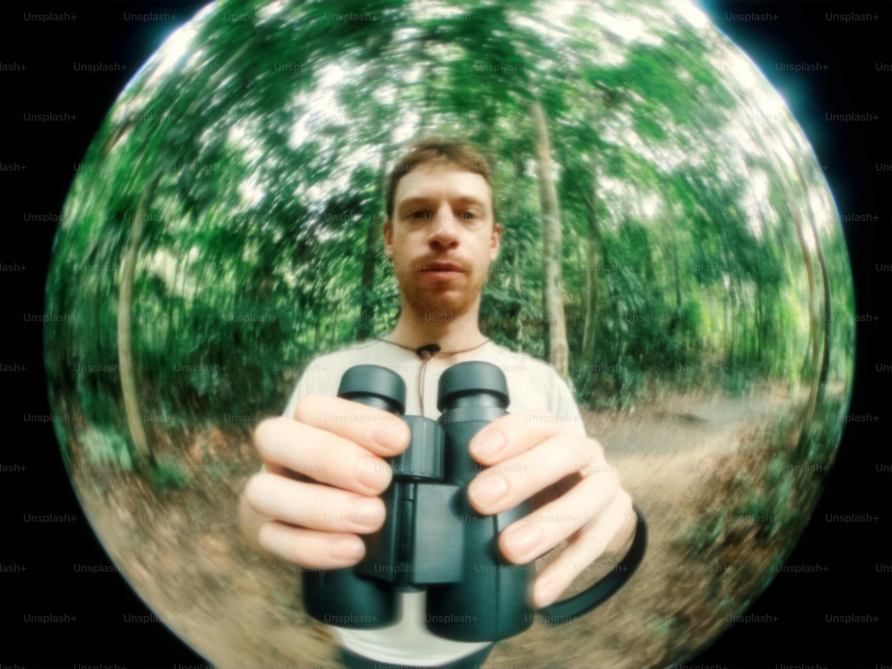 Homem segura binóculos na frente de uma floresta.