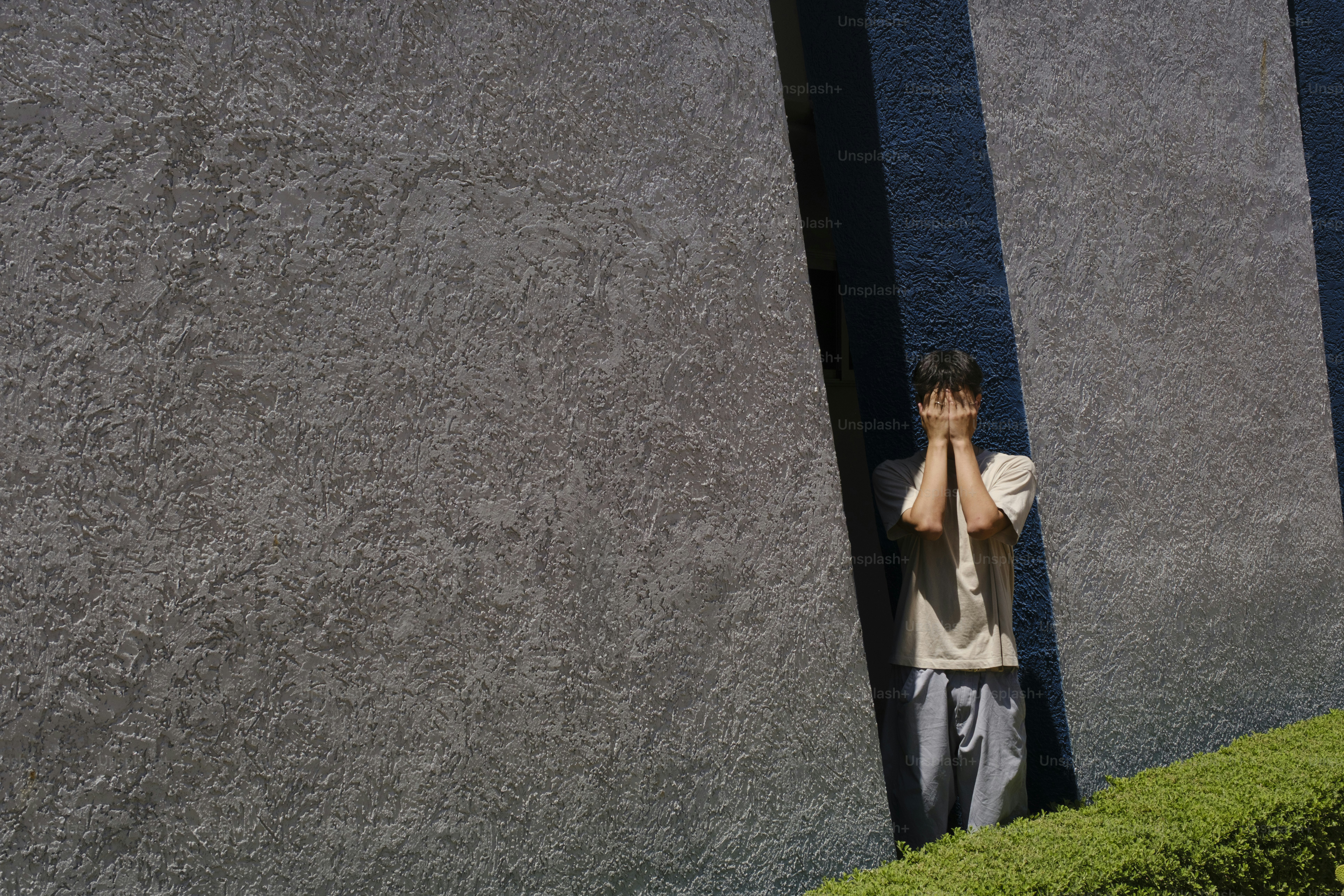 コンクリートの壁の近くで顔を覆う人。