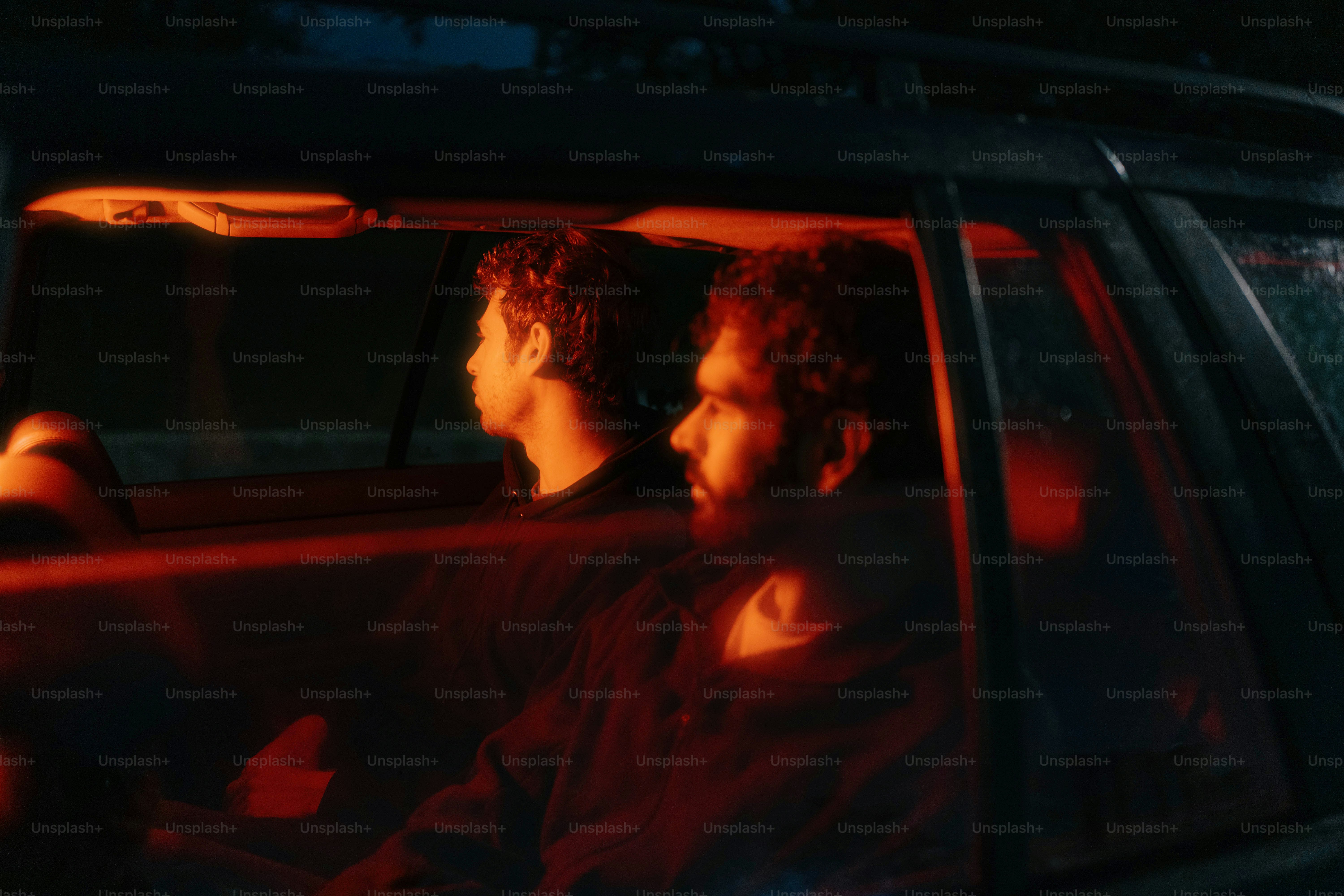Two men are in a car, illuminated by red light.