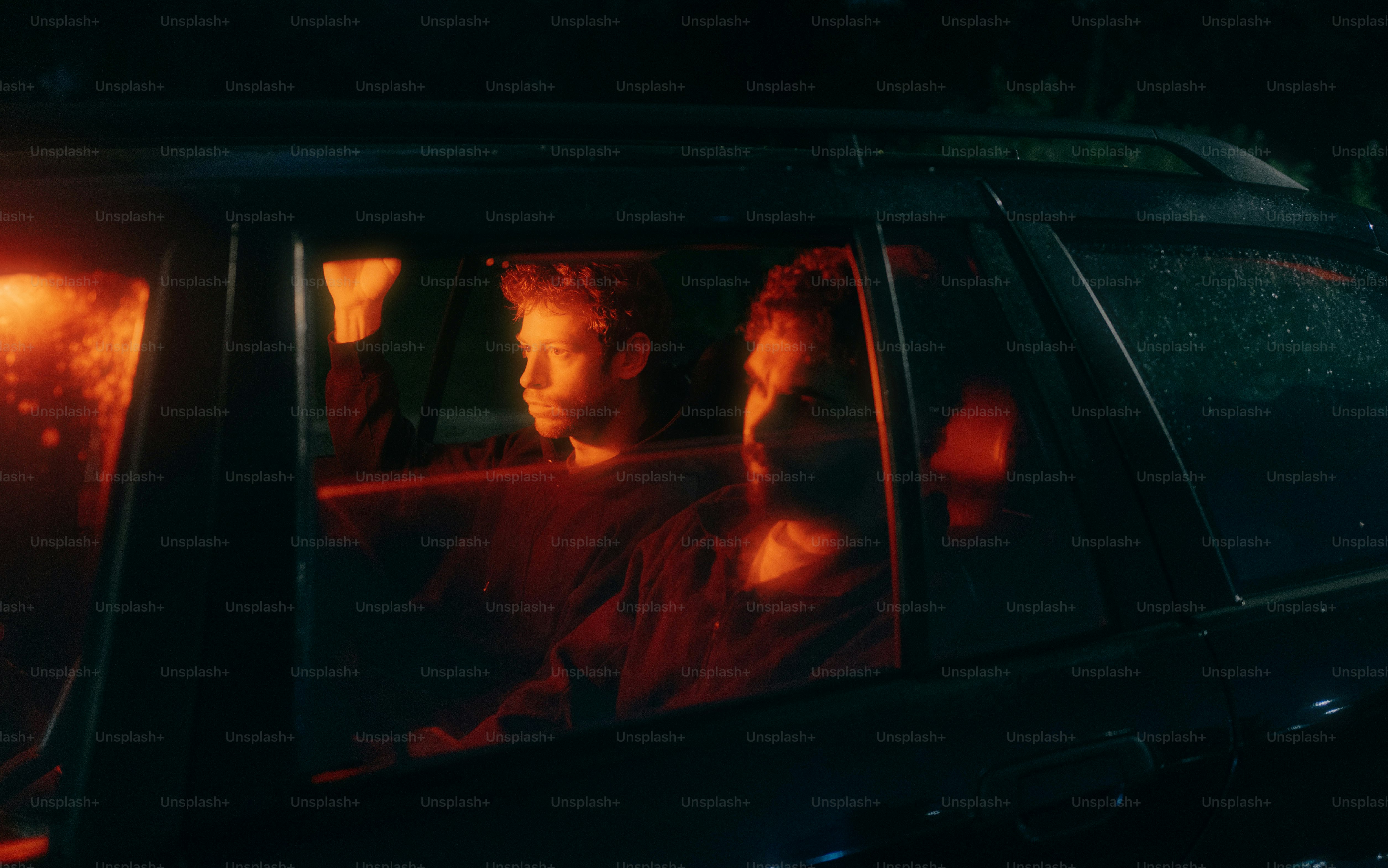 Two men are sitting in a dimly lit car.