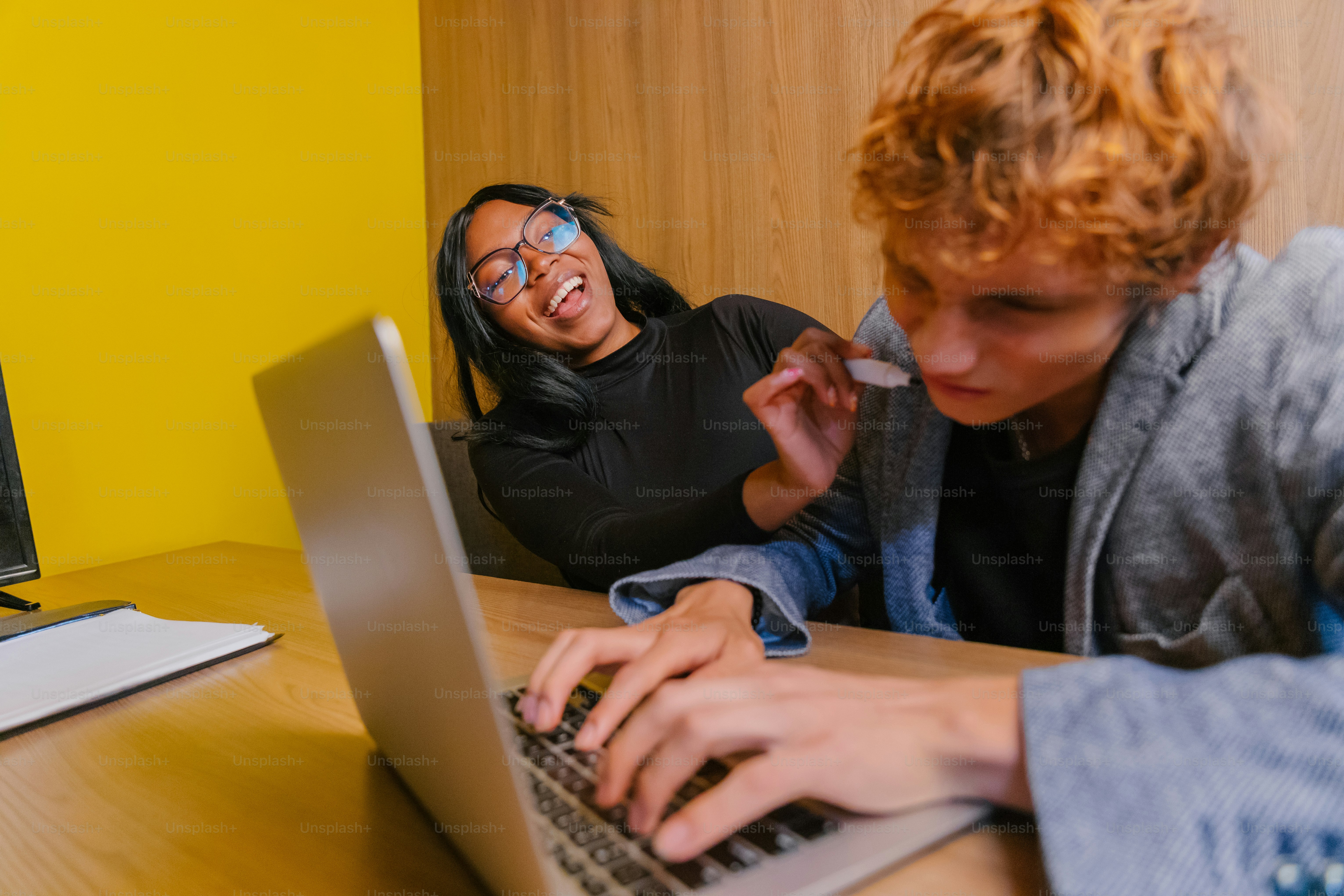 Seorang wanita tertawa sementara seorang pria bekerja di laptop.