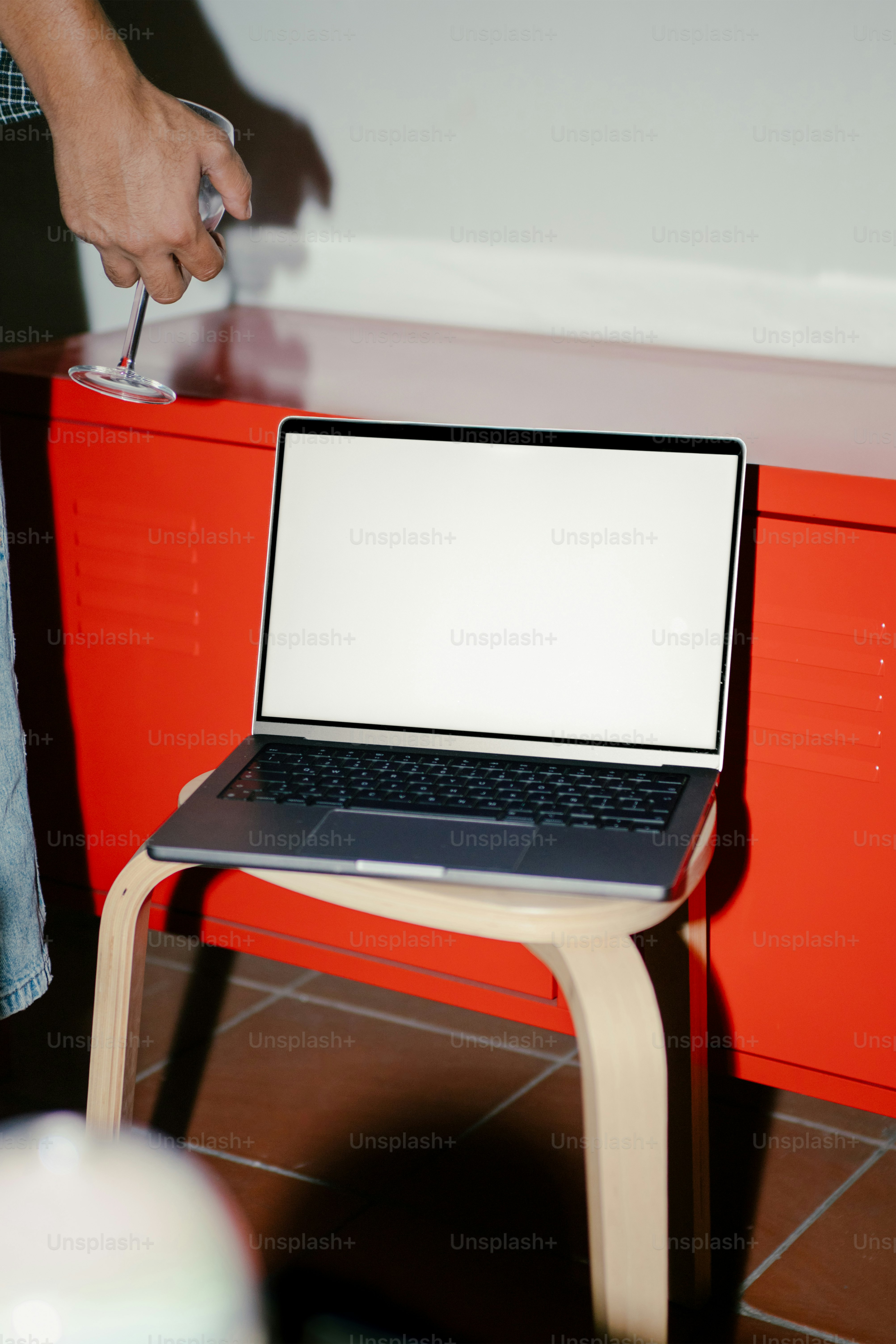 Laptop on a stool with someone holding a wine glass.