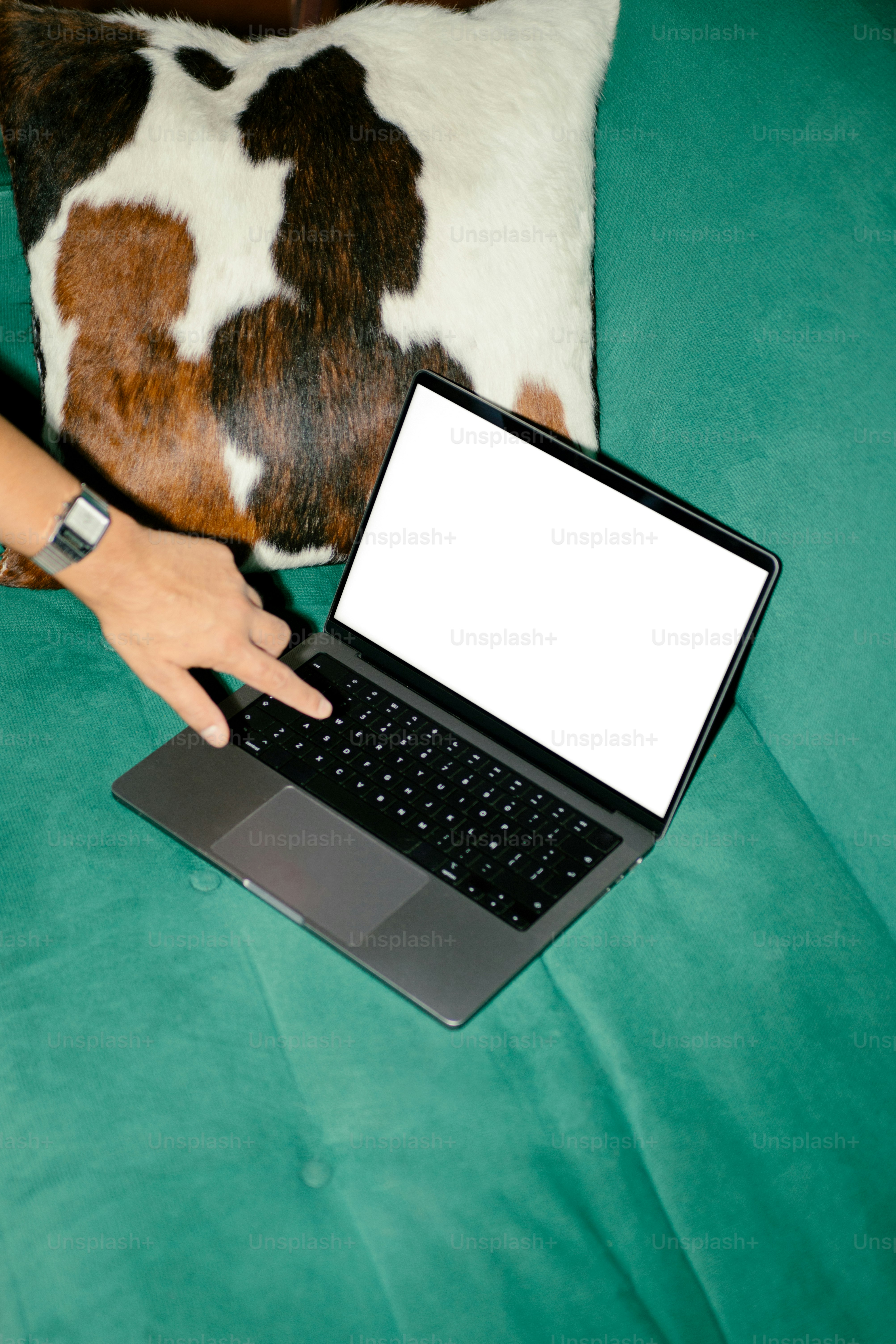 Person uses a laptop on a teal sofa.