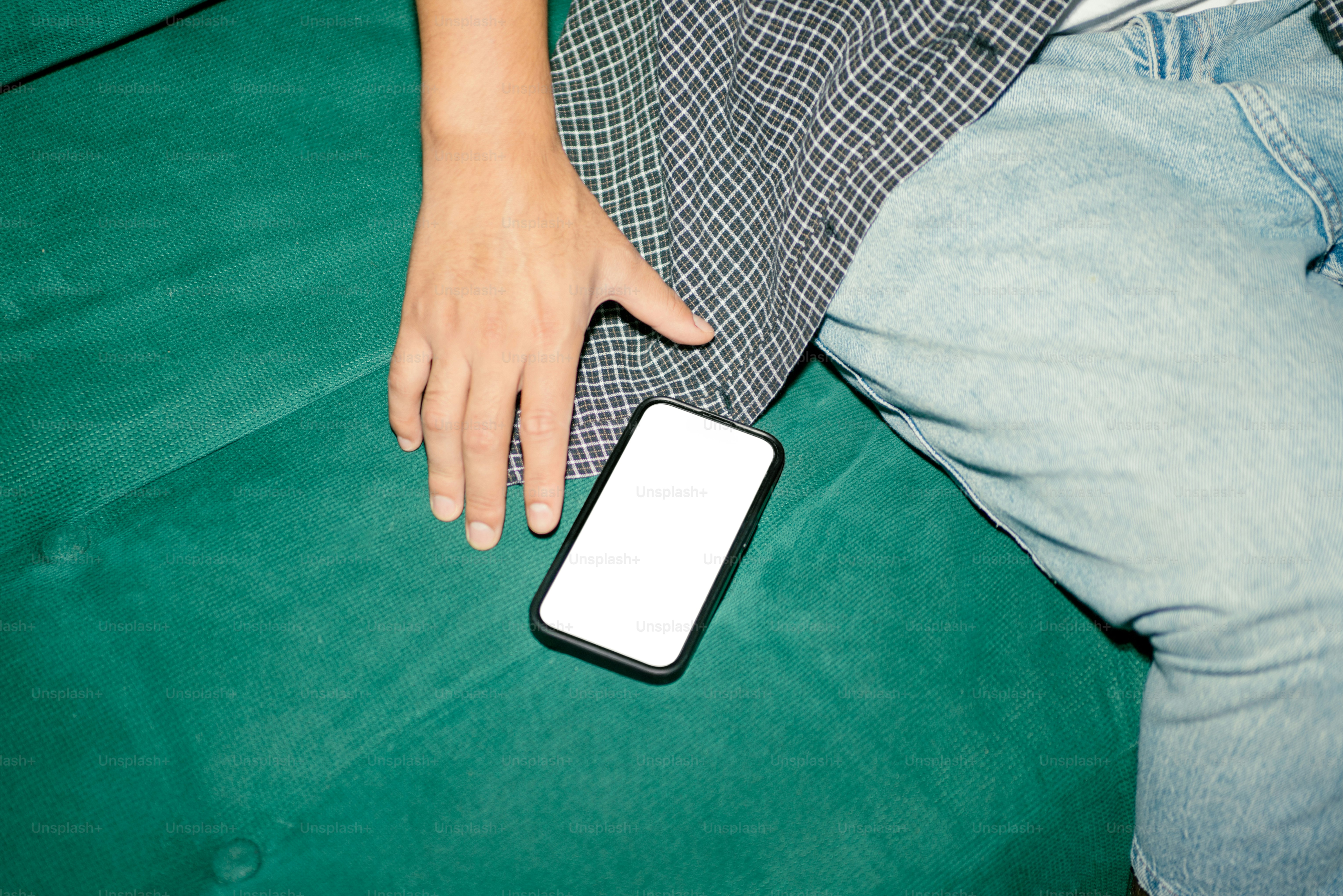 A hand rests near a phone on a green surface.