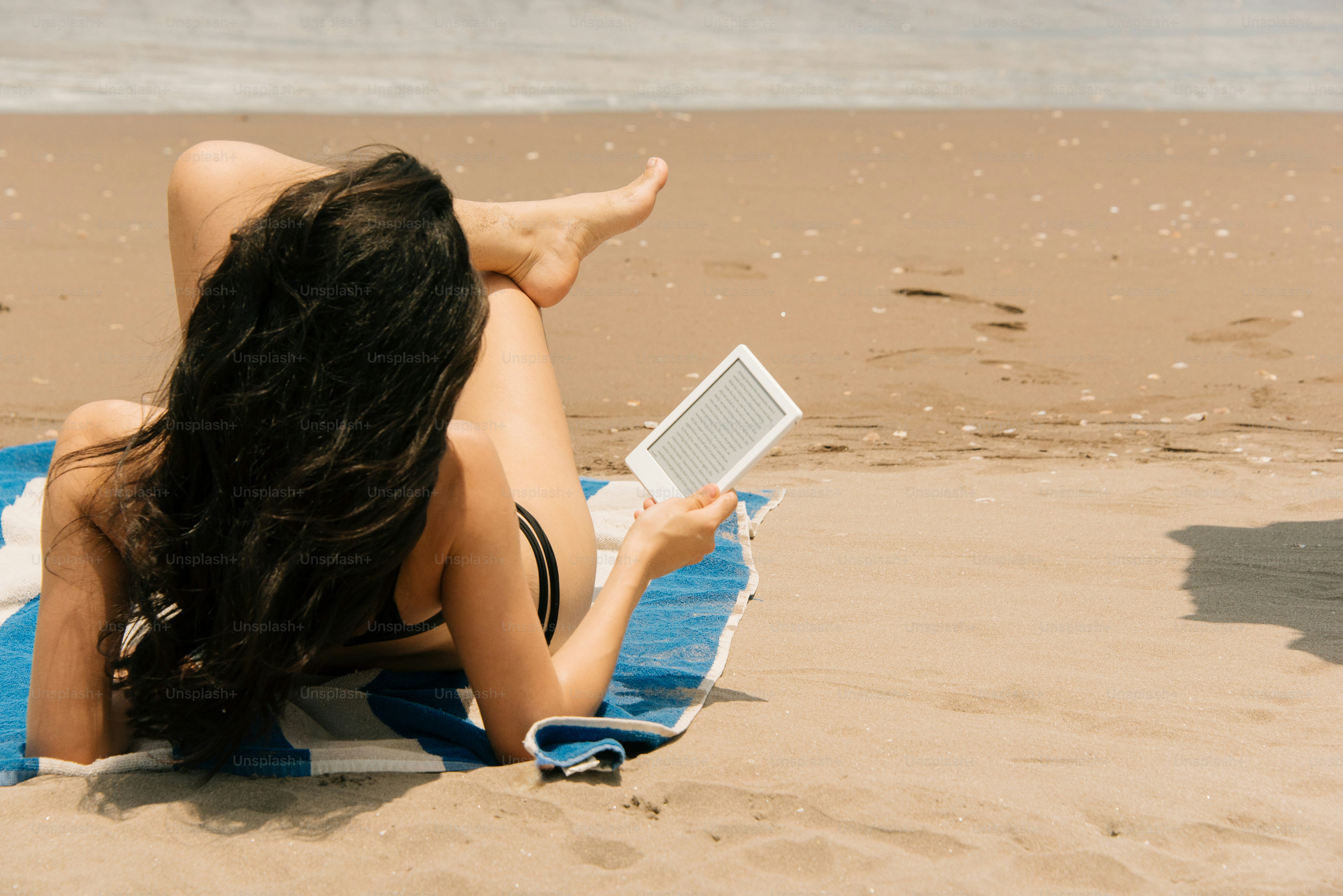 Donna che legge un e-reader mentre prende il sole sulla spiaggia.