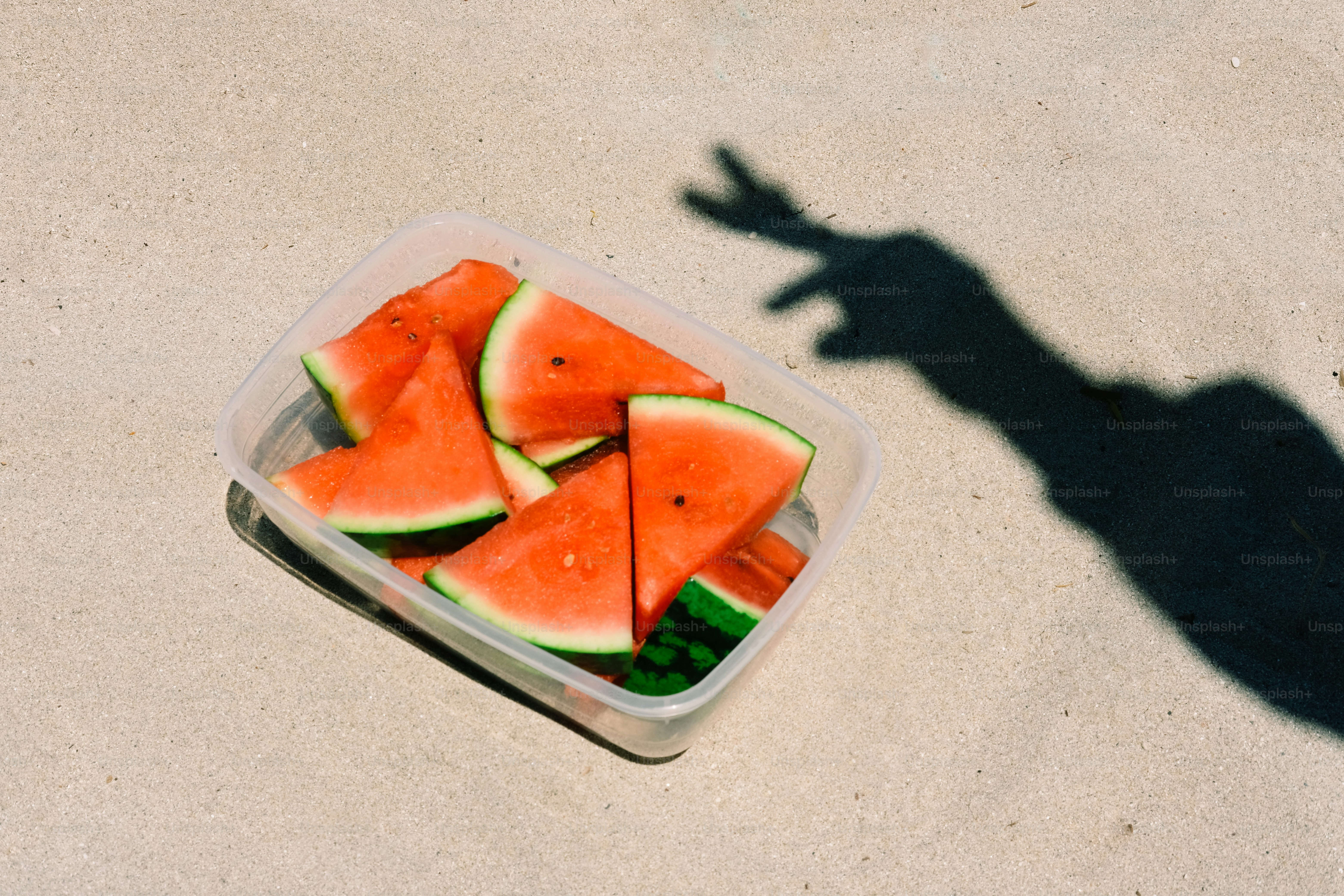 Watermelon slices in a container with a hand shadow.