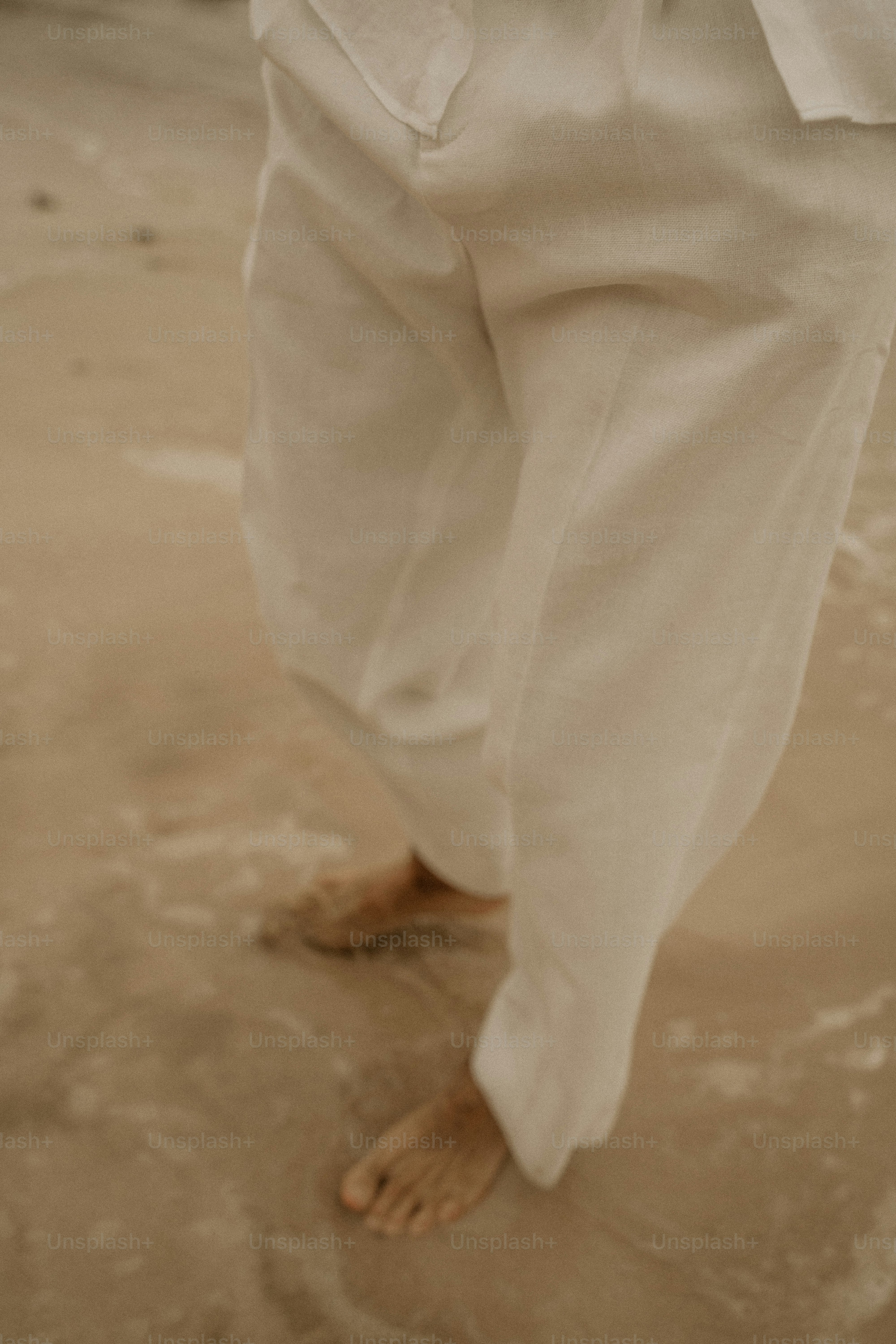 Person, die am Strand spazieren geht und weiße Hosen trägt.