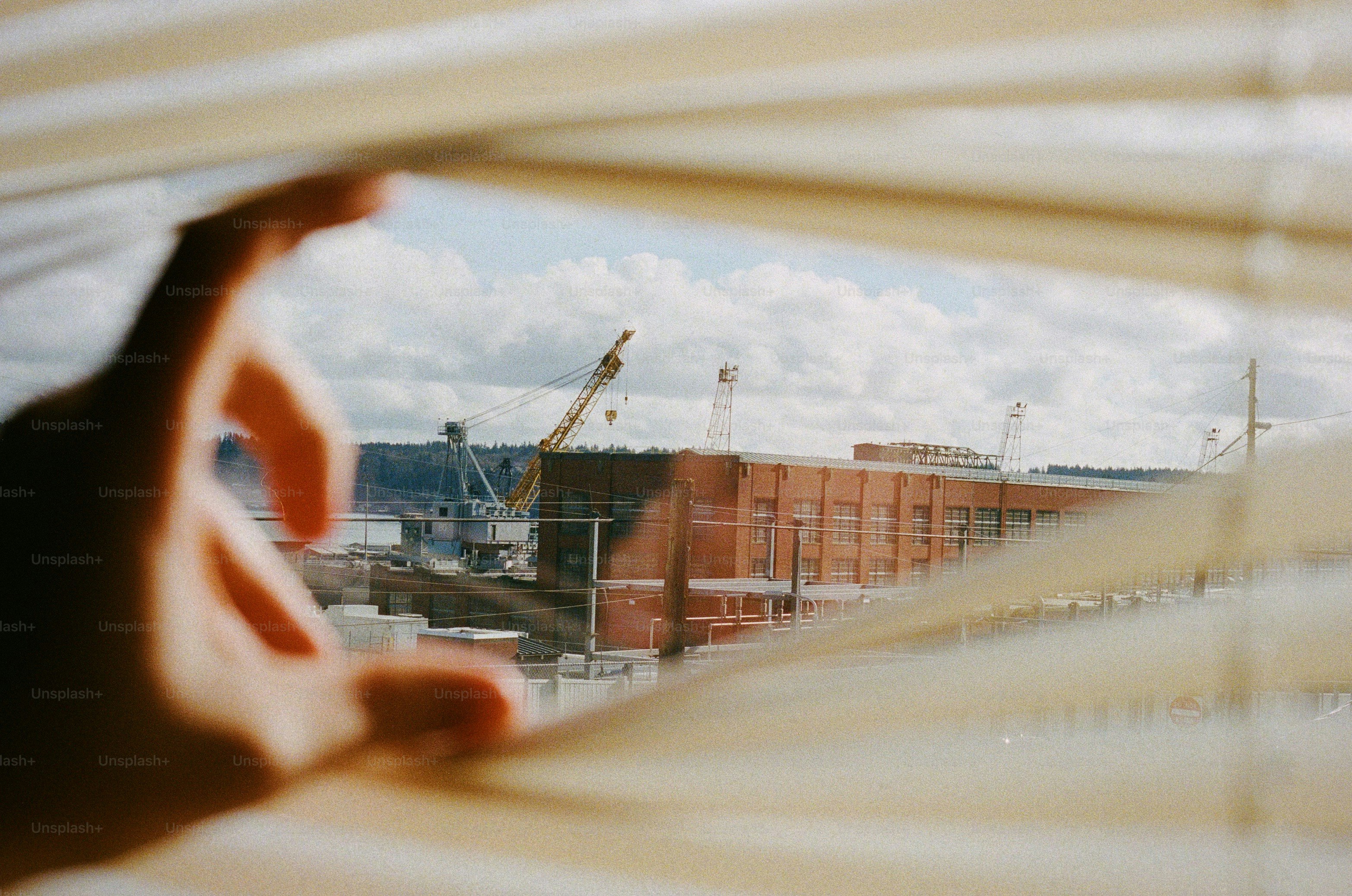 Hand peeks through blinds, looking at a shipyard.