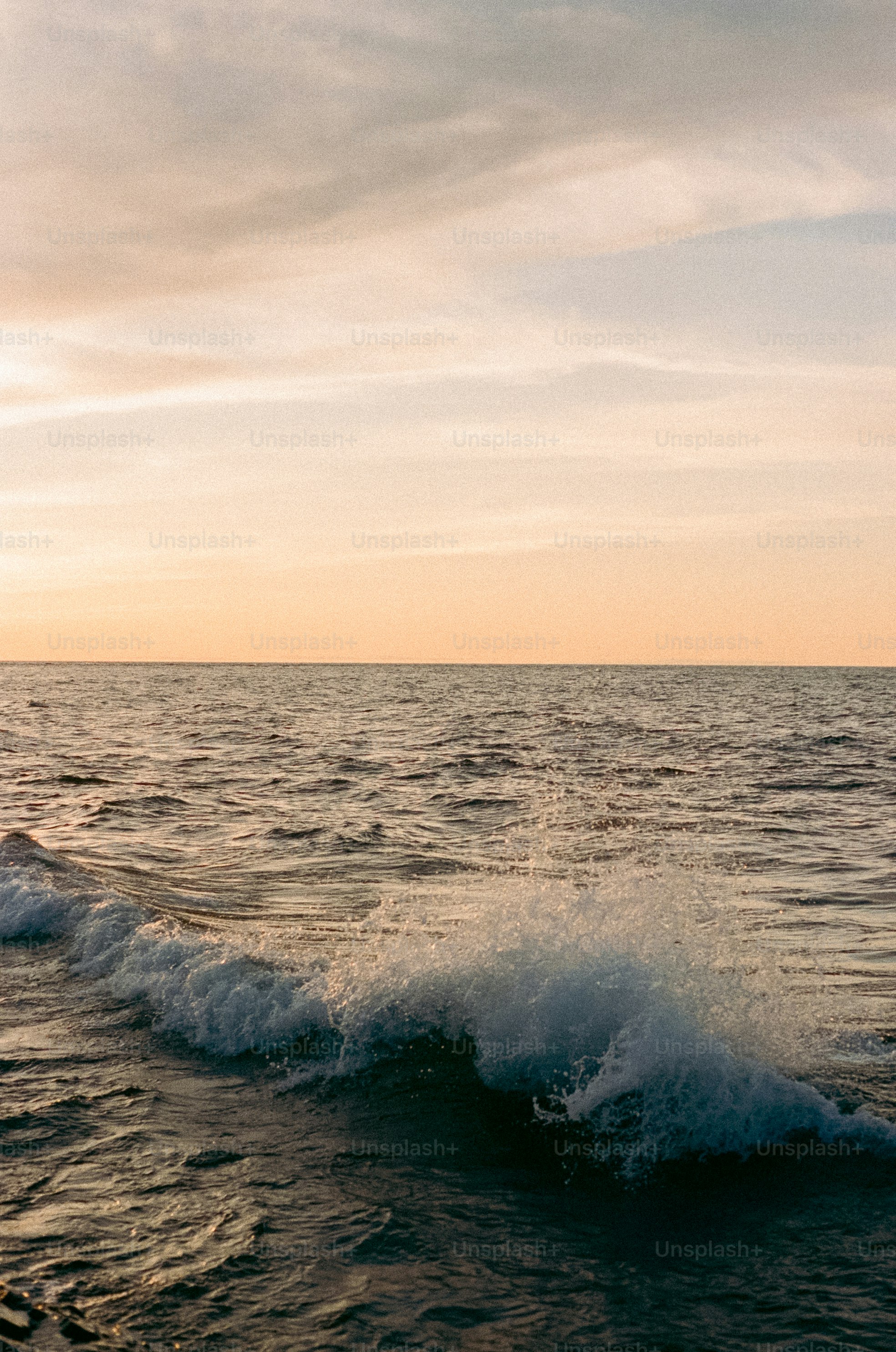 Gentle waves crash on a beach at sunset.