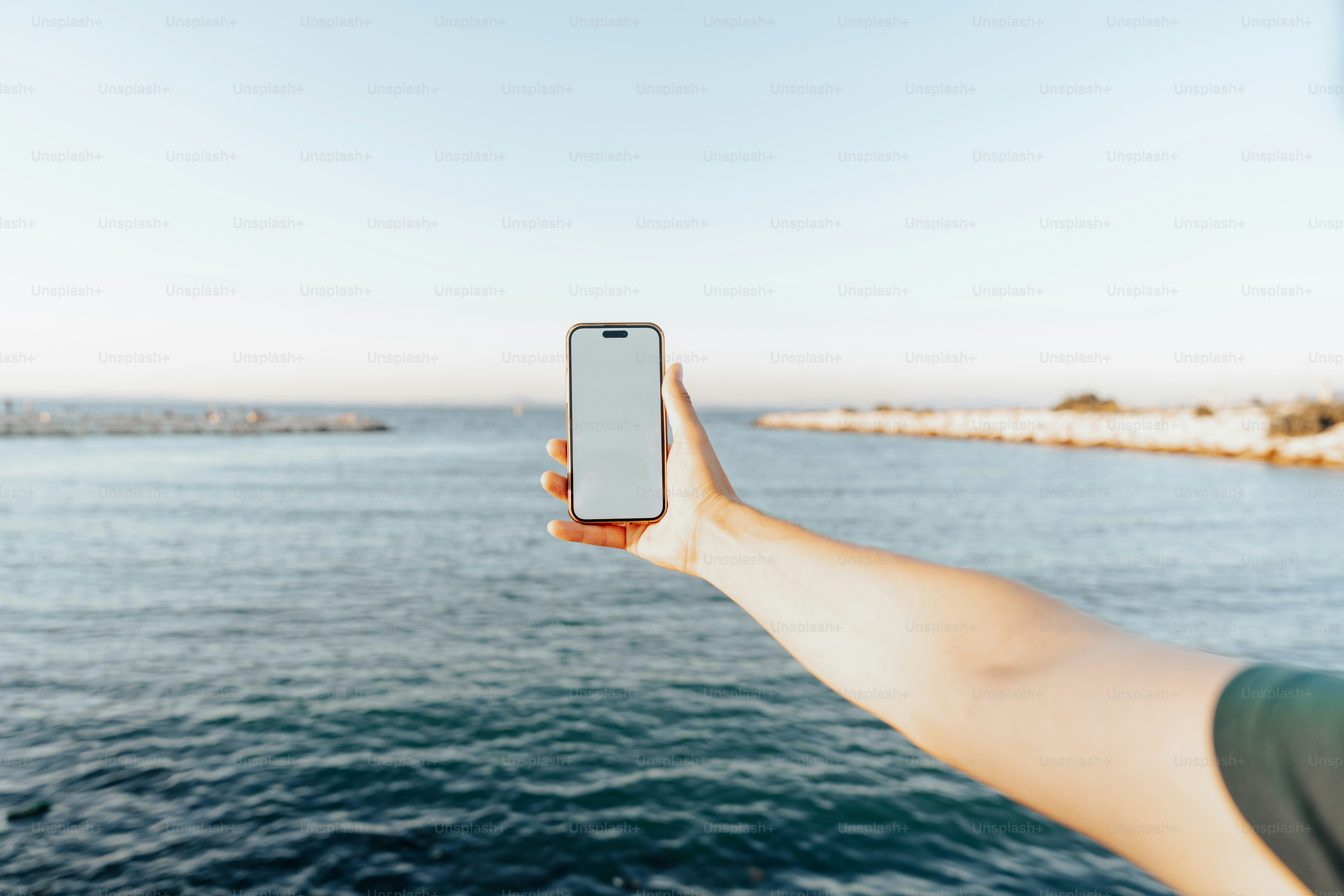 海を背景に電話を持つ手。