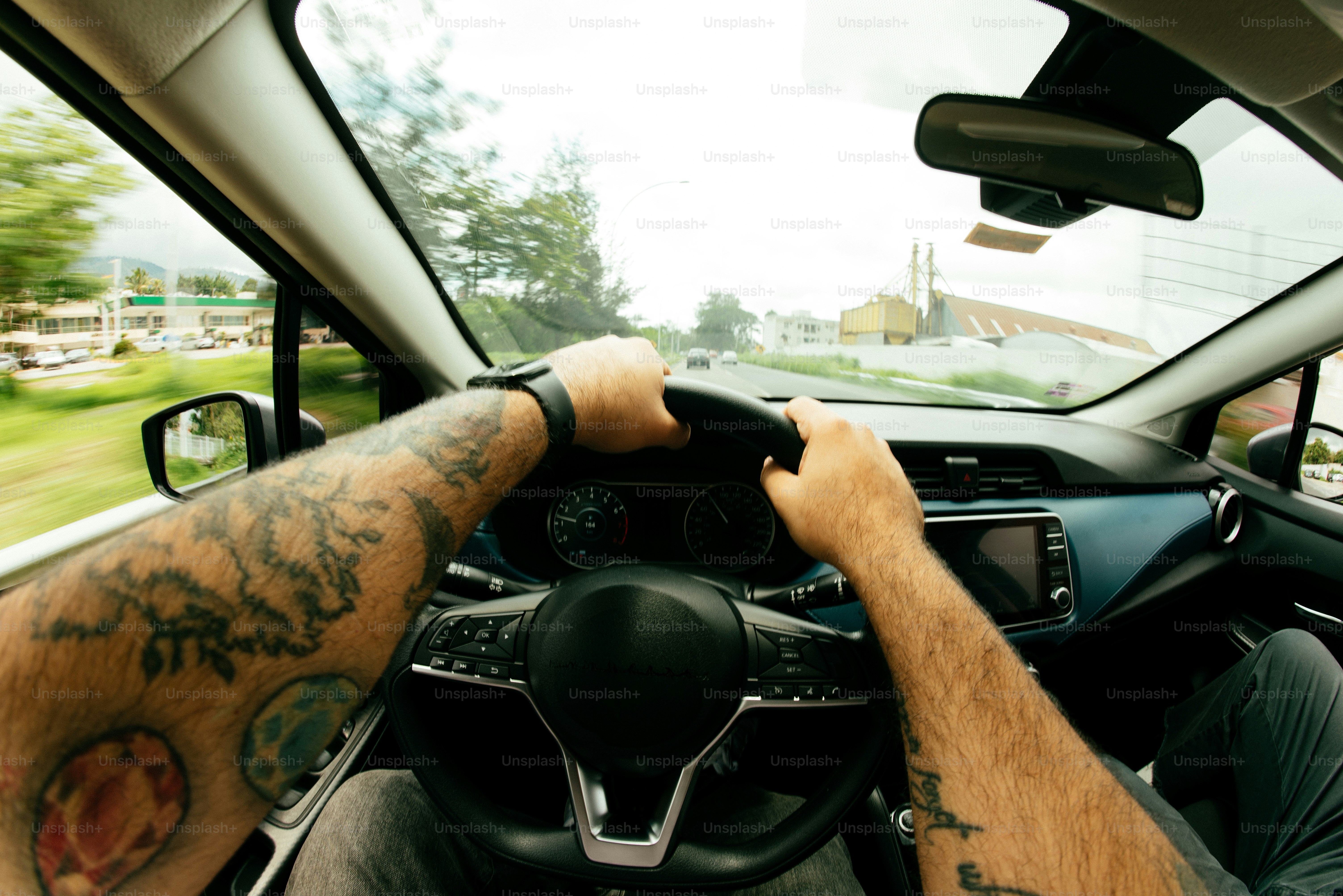 Someone with tattoos is driving a car.