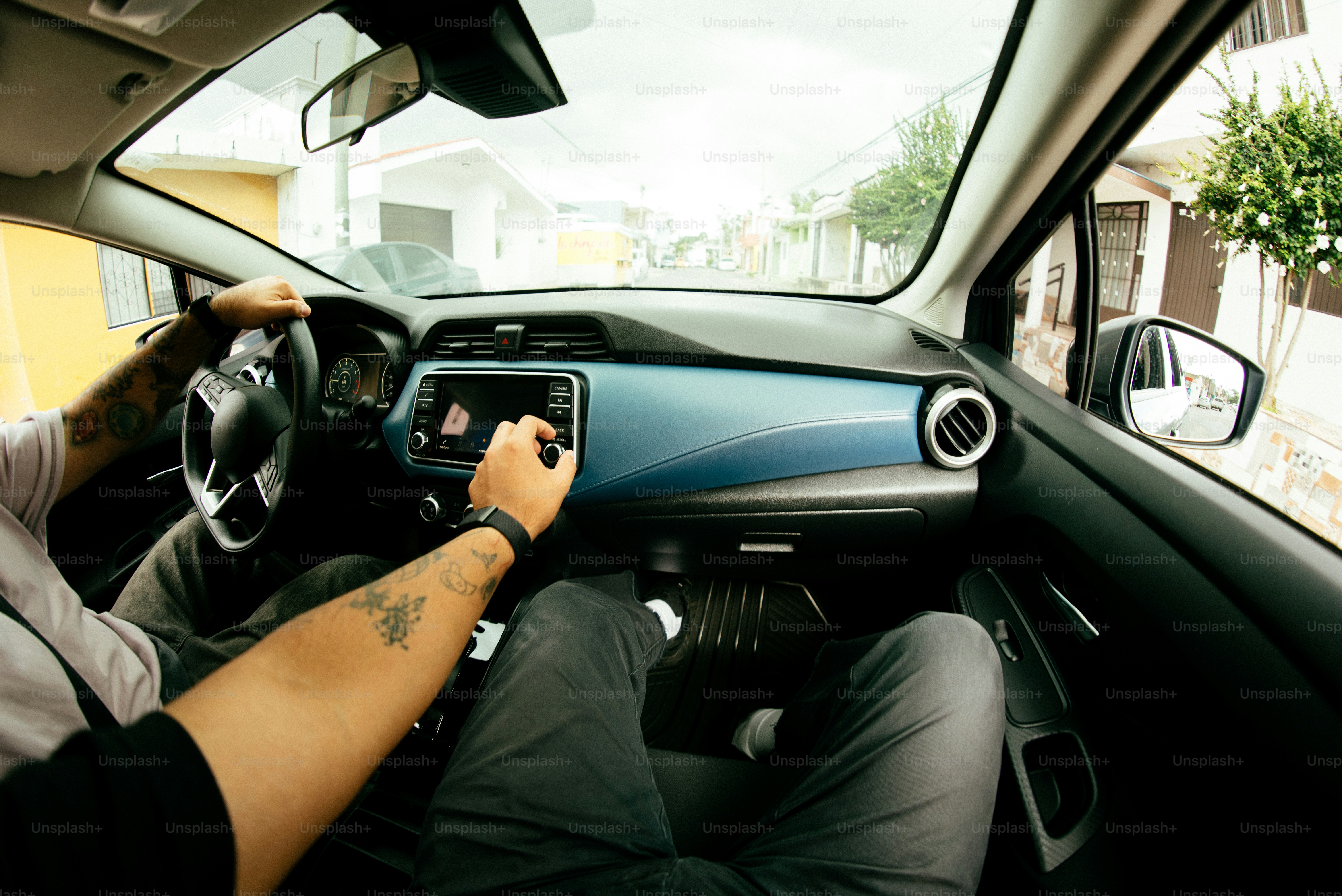 A person drives a car with visible tattoos.