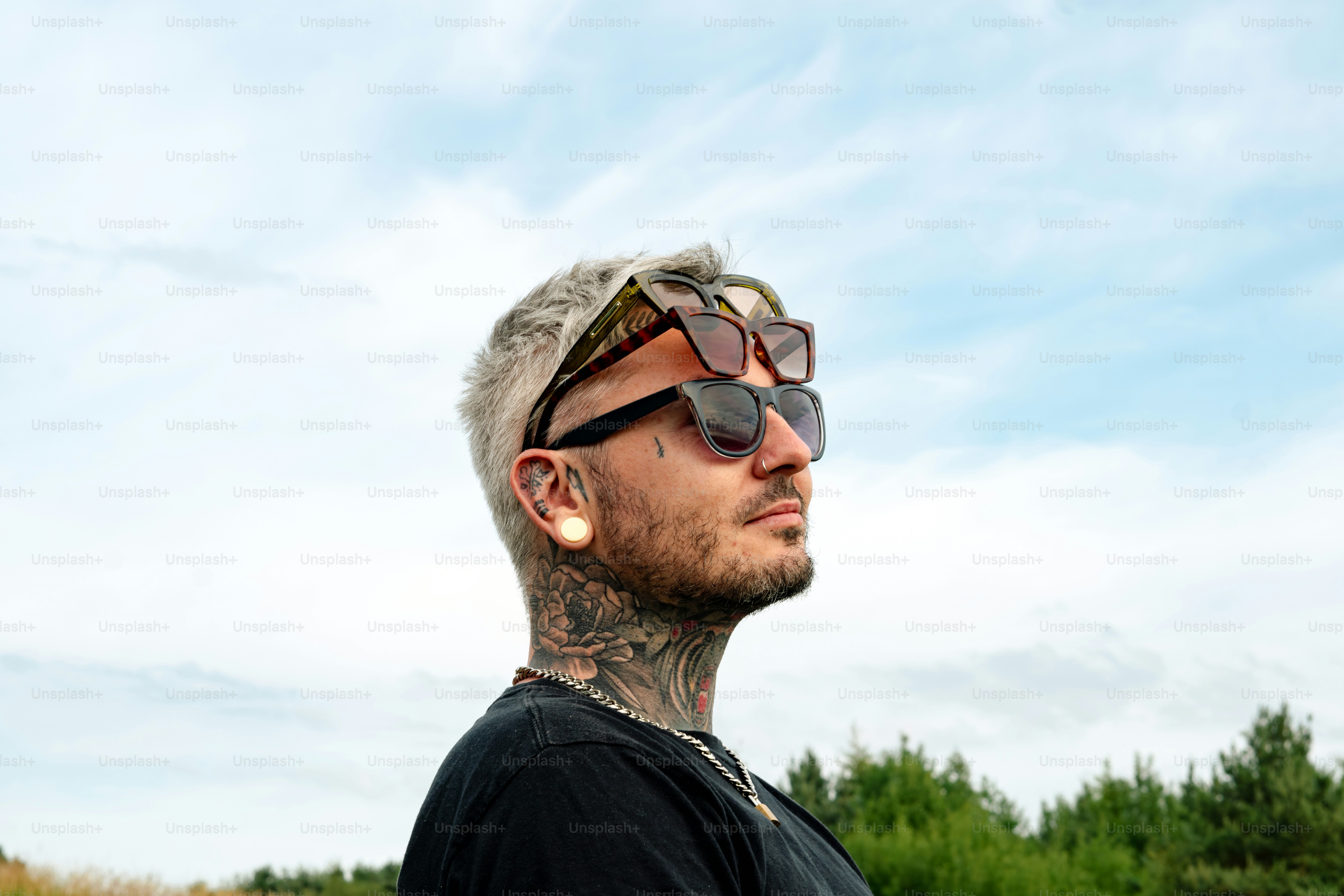 Man with tattoos and sunglasses gazes upward.