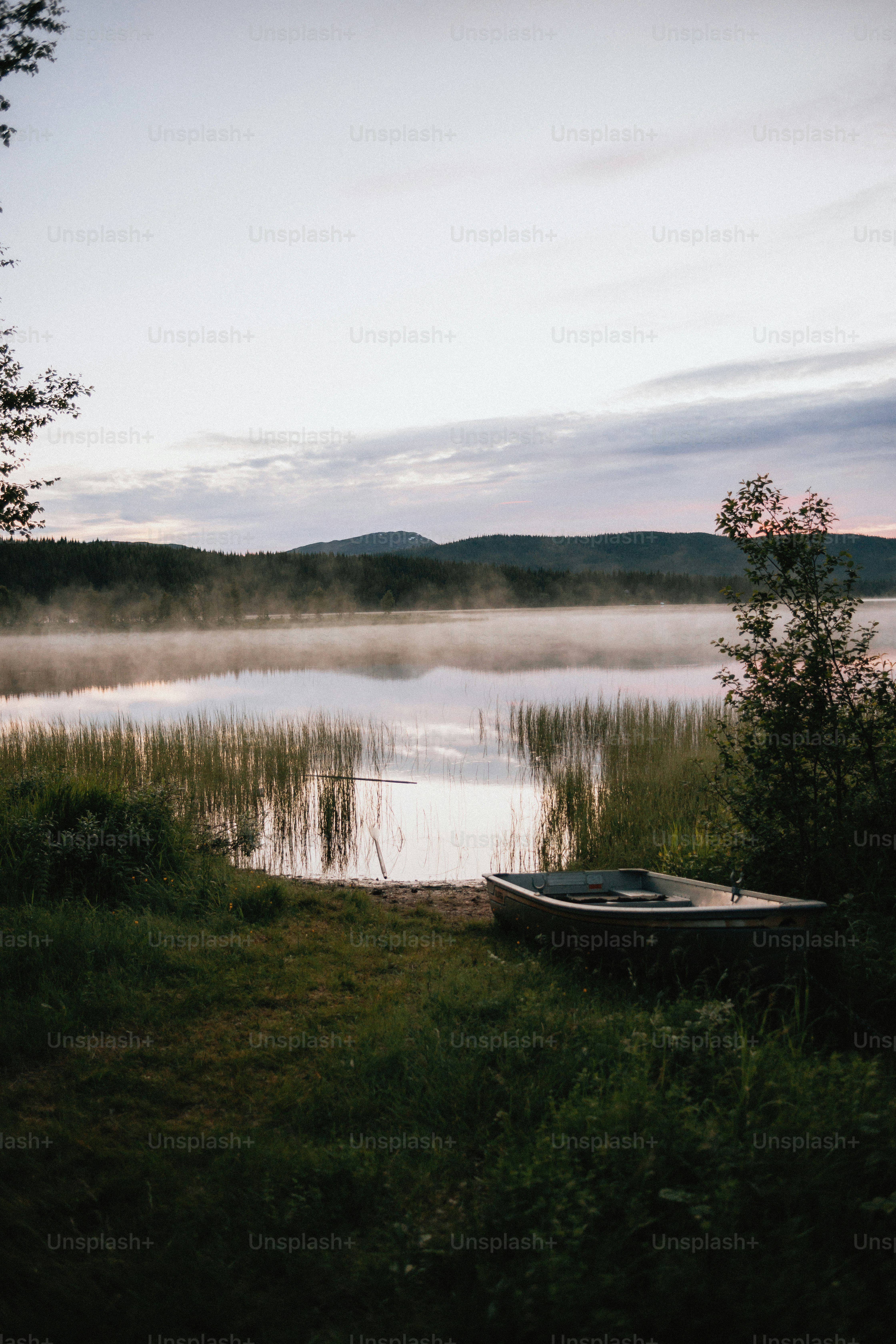 Ein Boot liegt in der Abenddämmerung neben einem nebligen See.