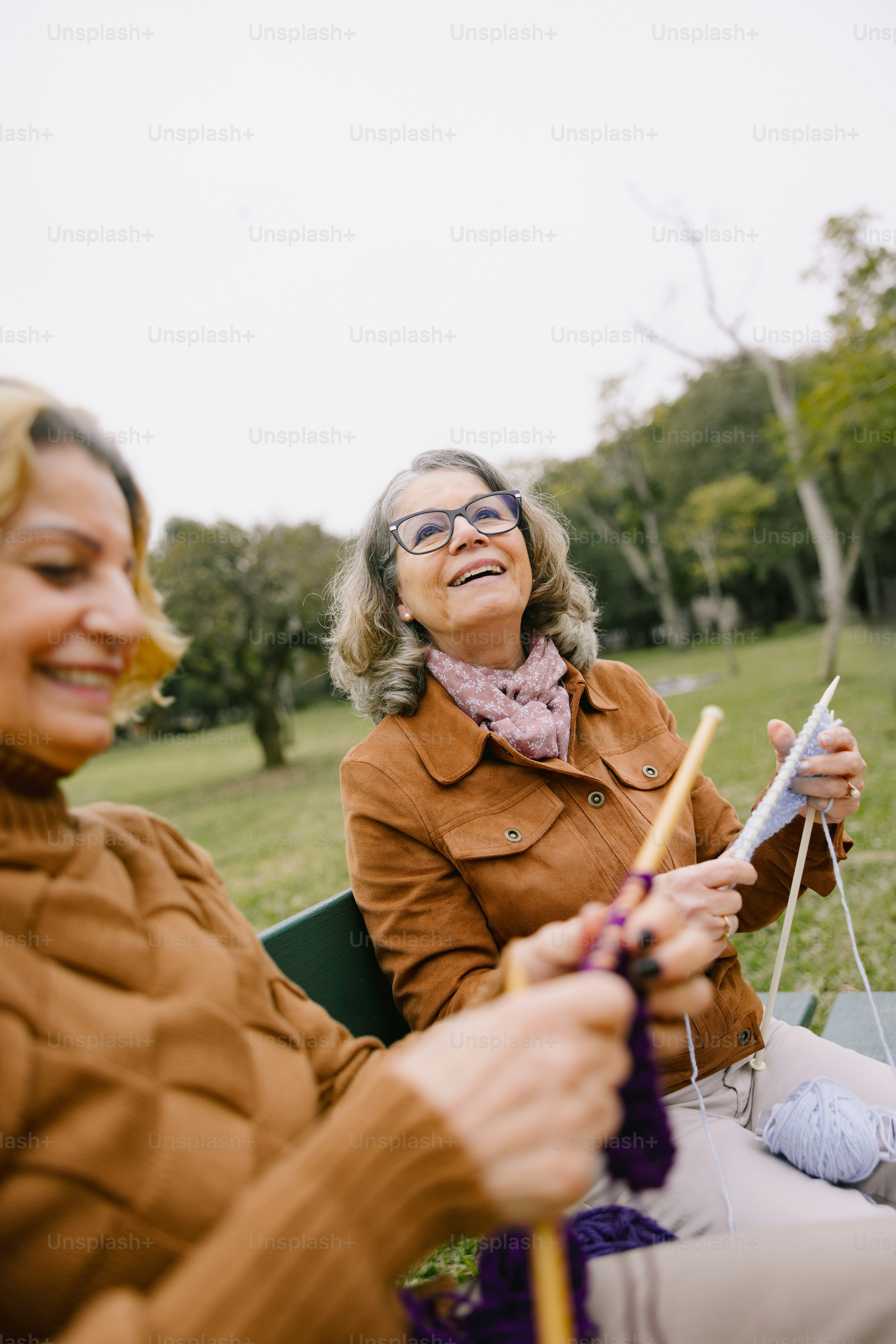 Two smiling women knit outside in the park.