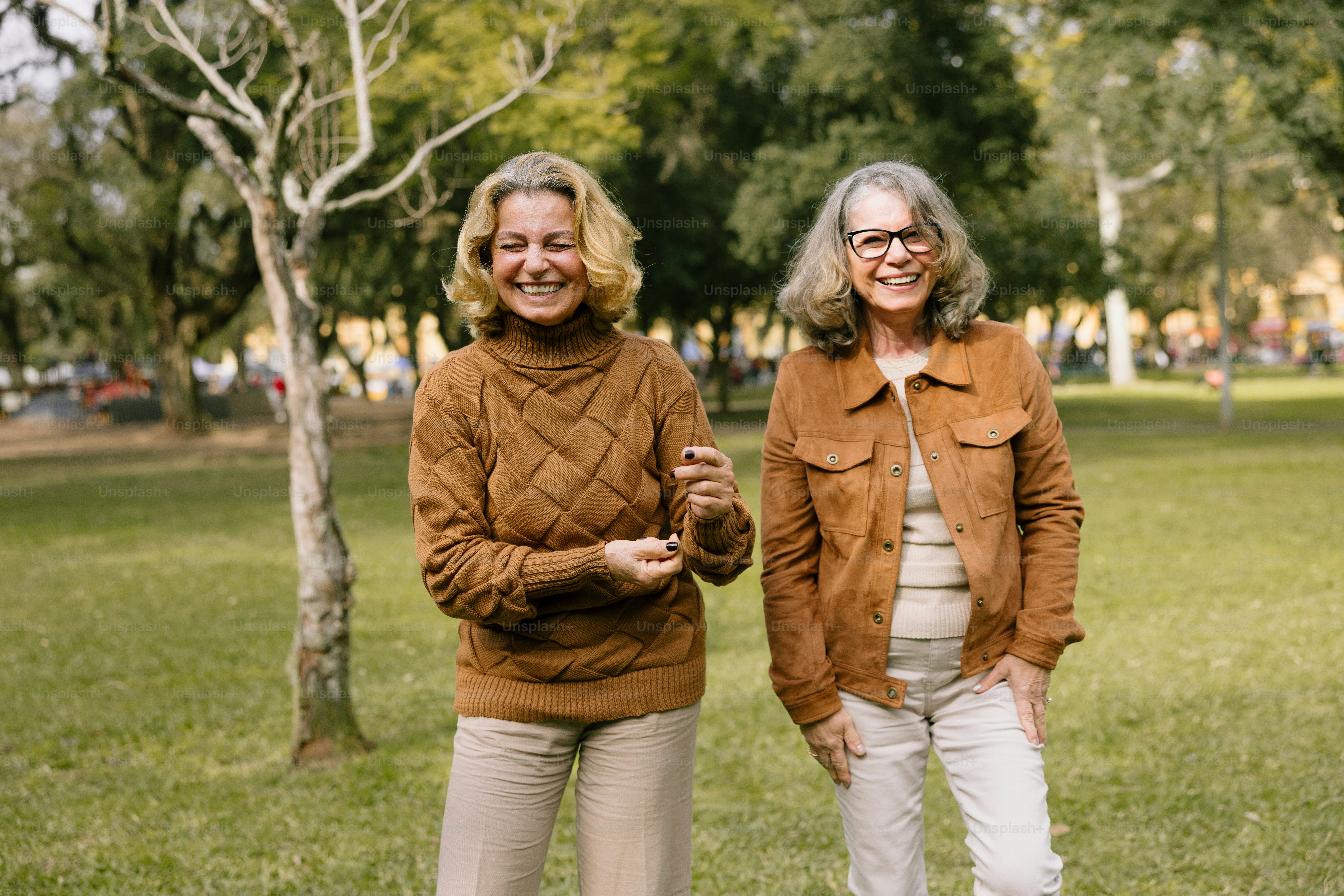 Two smiling women pose together outside in a park.