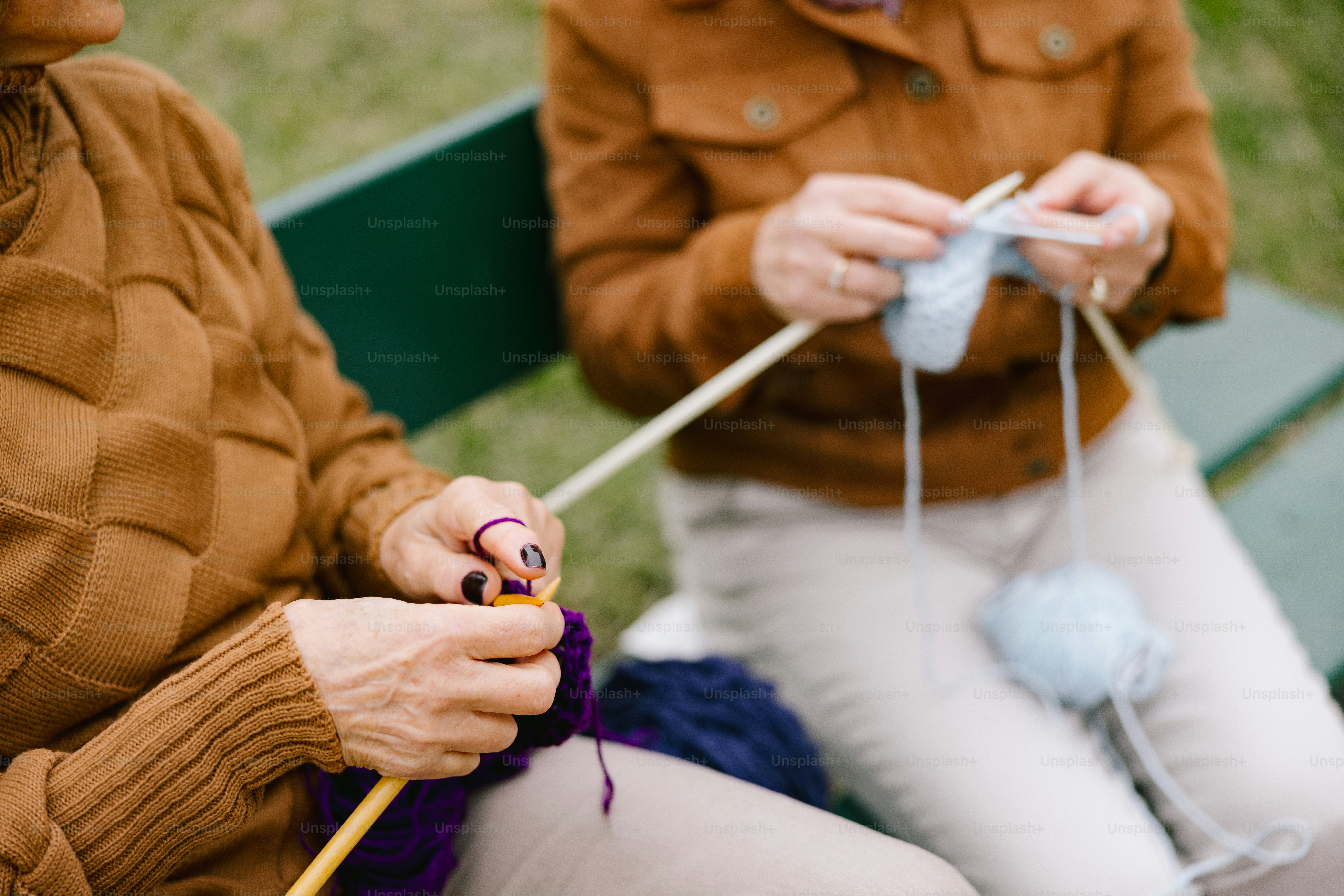 Two women are knitting together outdoors.