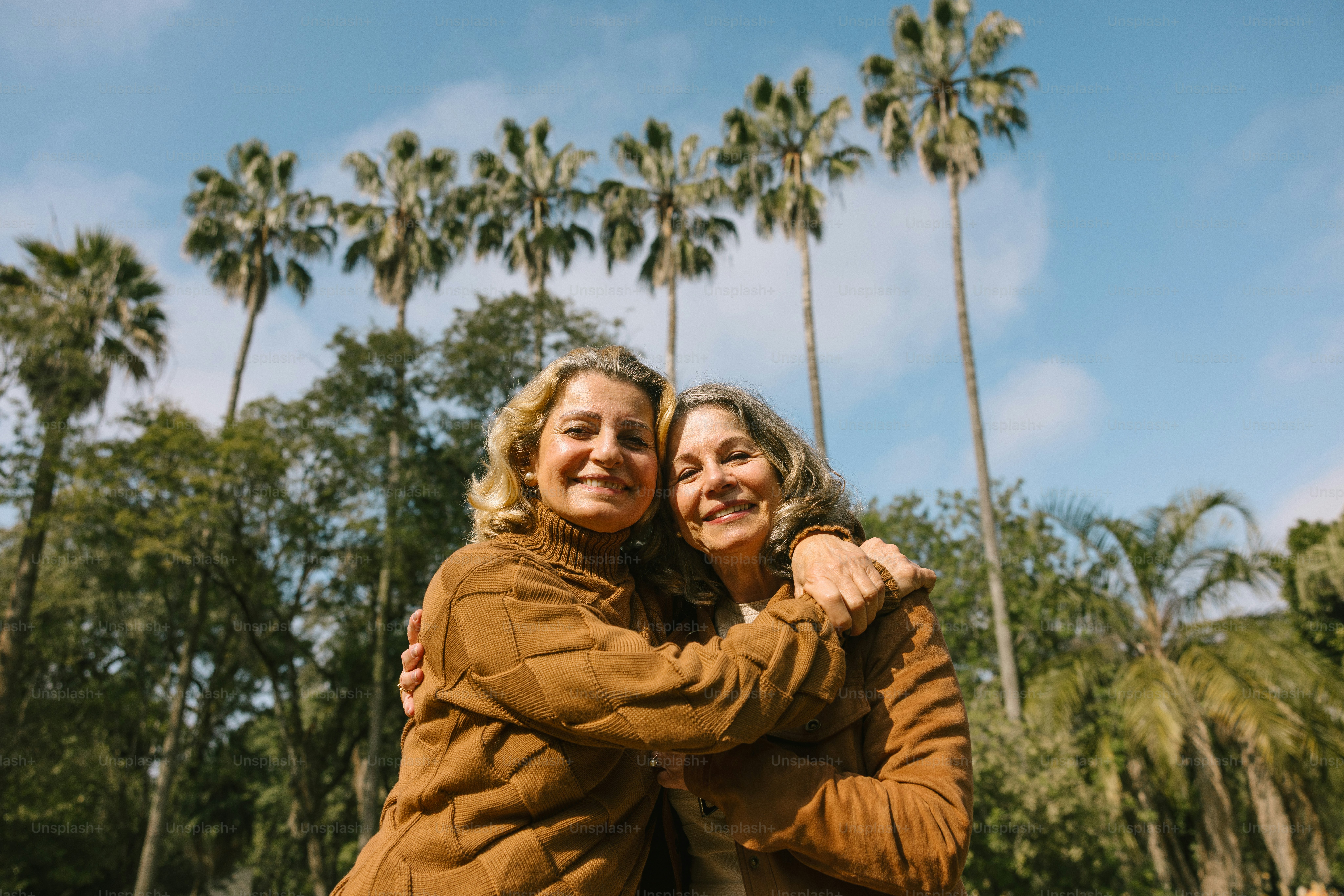 Two women embrace in front of palm trees.