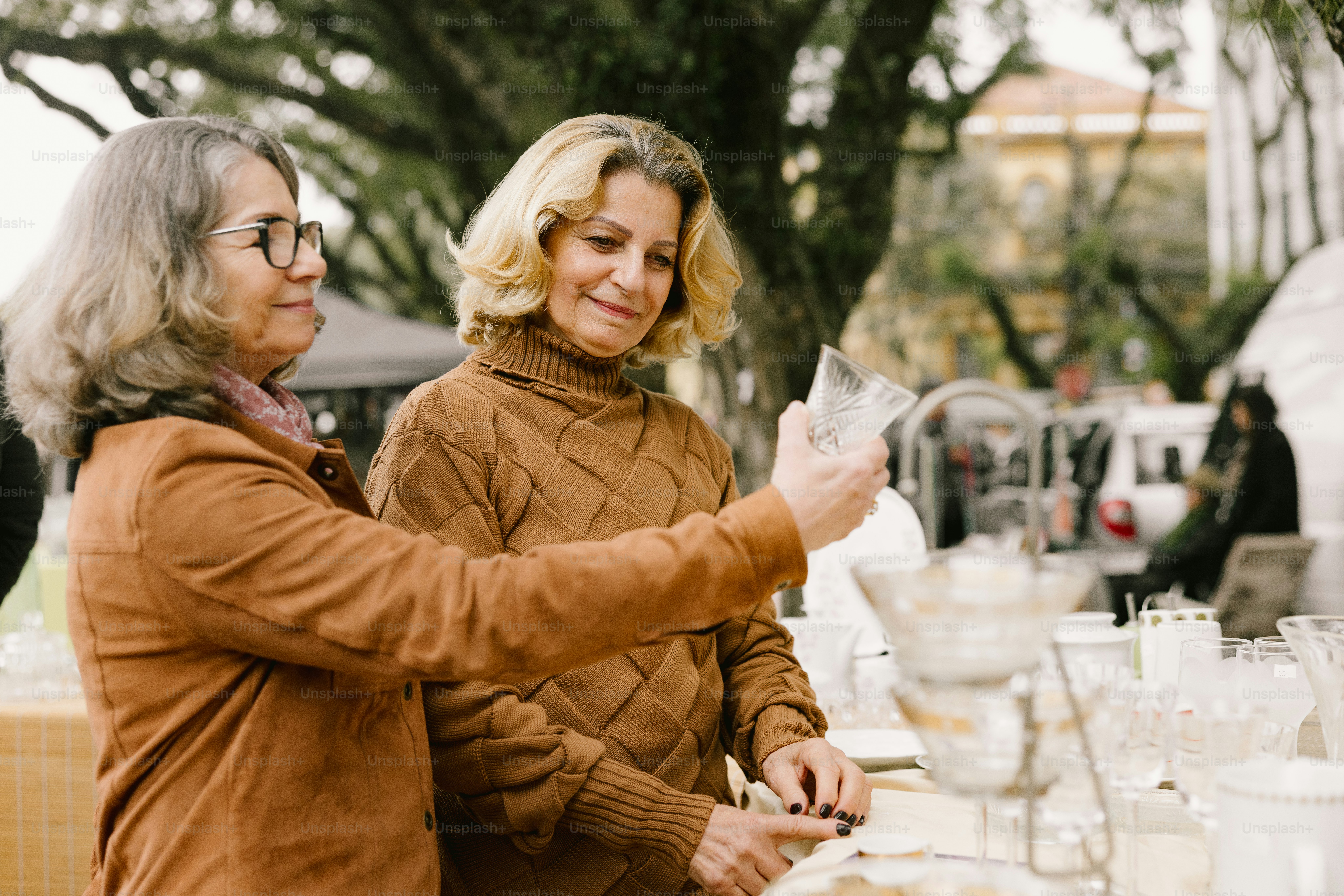 Two women examine glassware at an outdoor event.