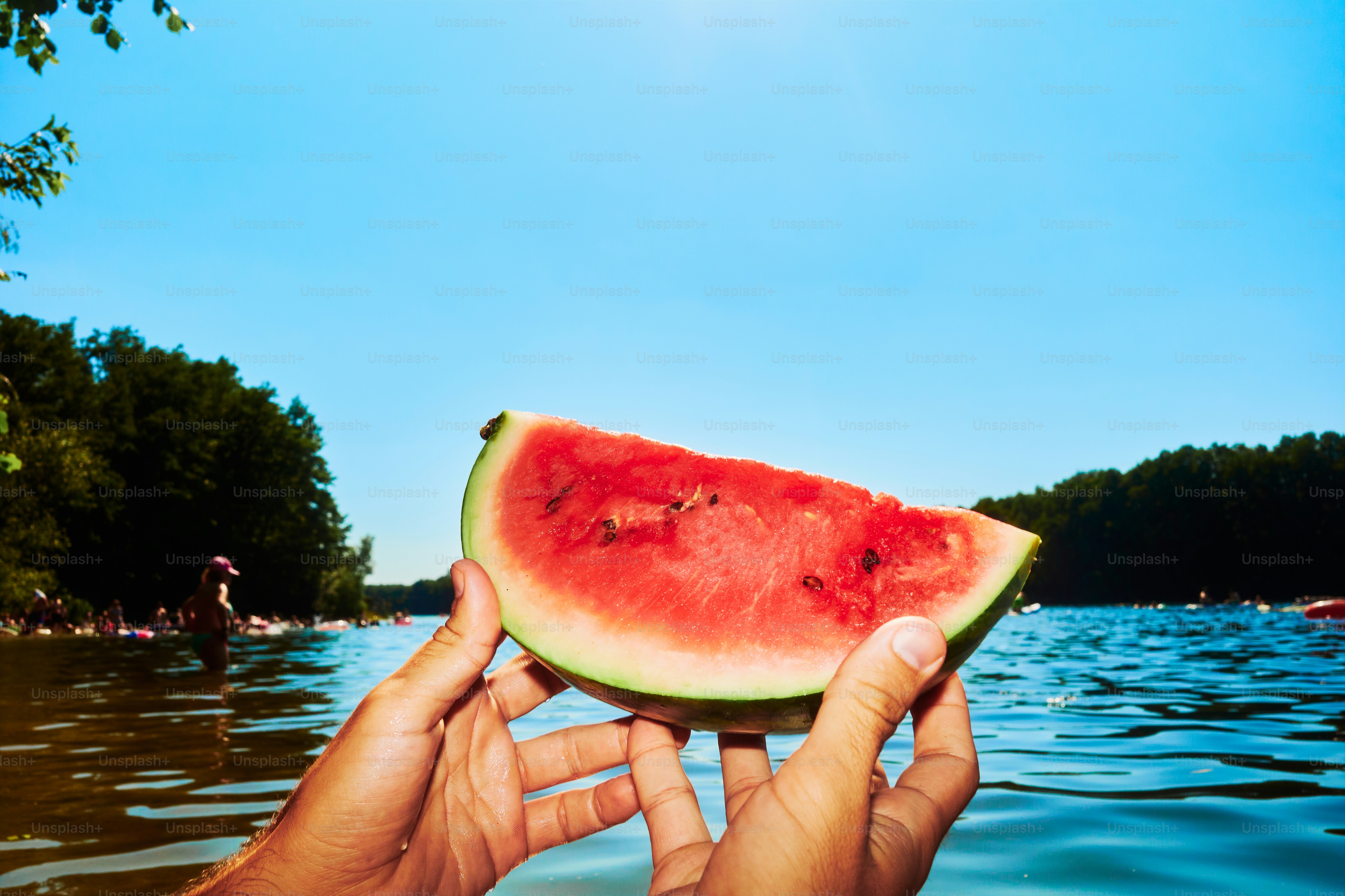 Hands hold a watermelon slice by the water