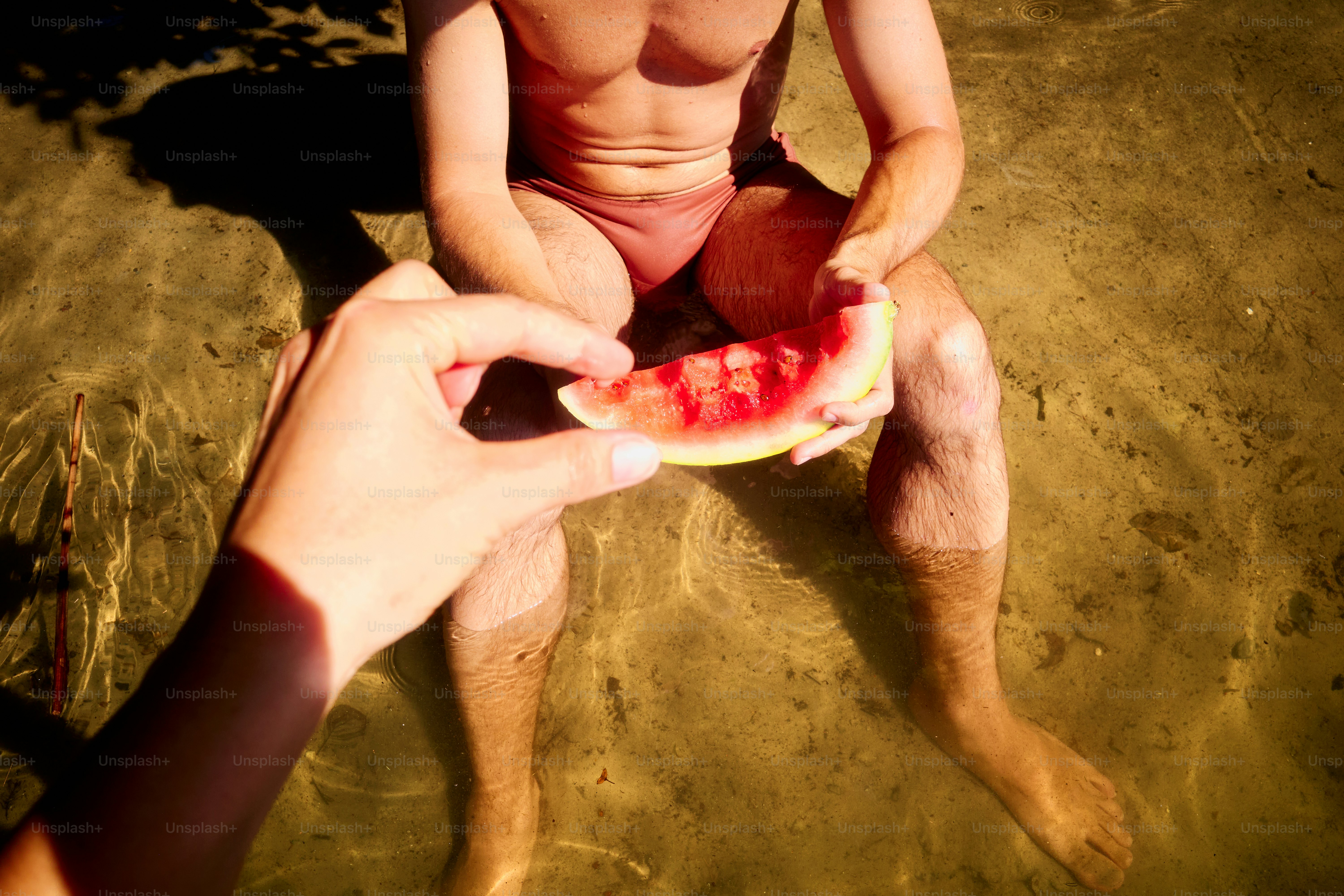 Jemand bietet einem Mann im Wasser eine Wassermelone an.