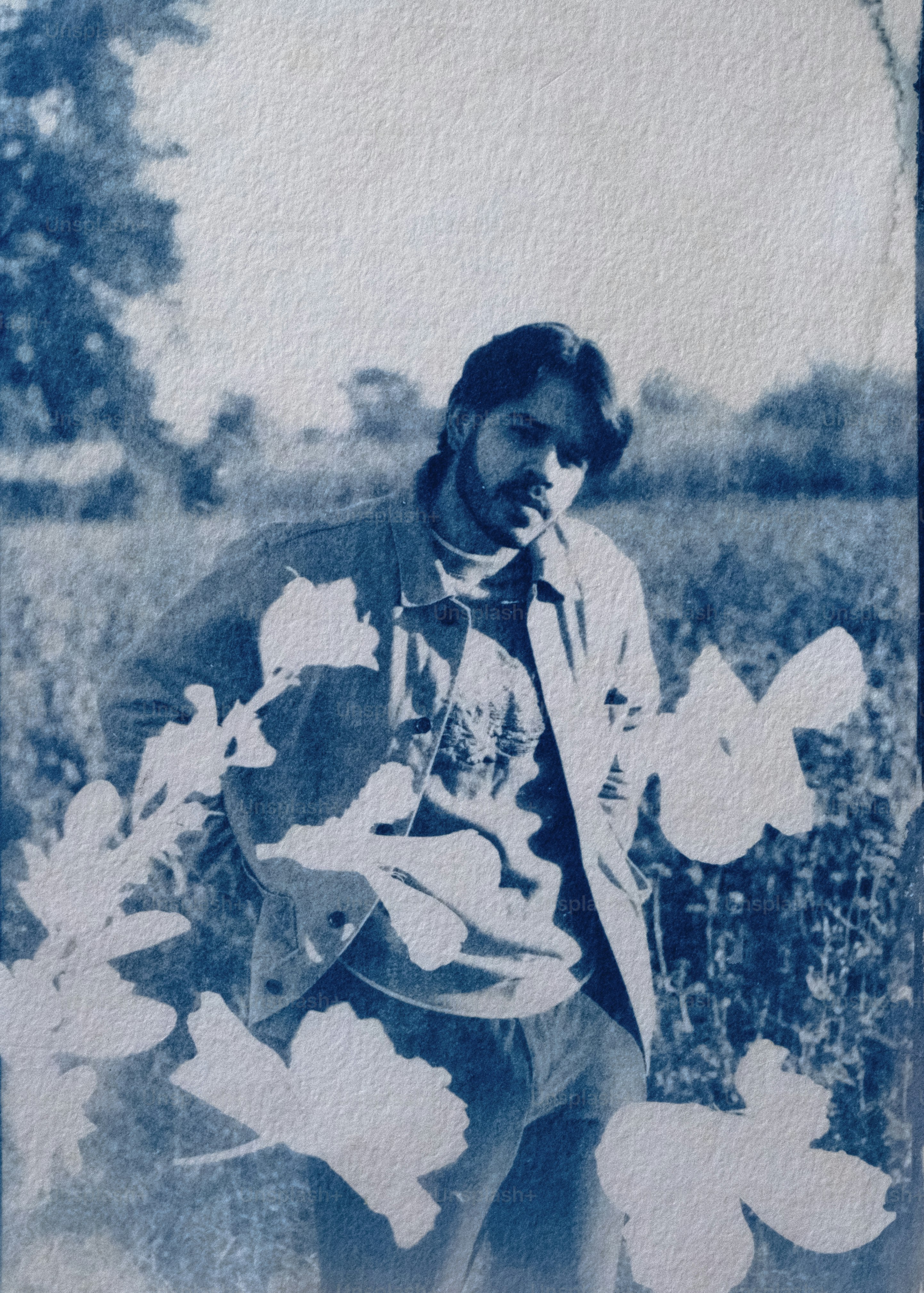Un hombre posa al aire libre, parcialmente oscurecido por las flores.