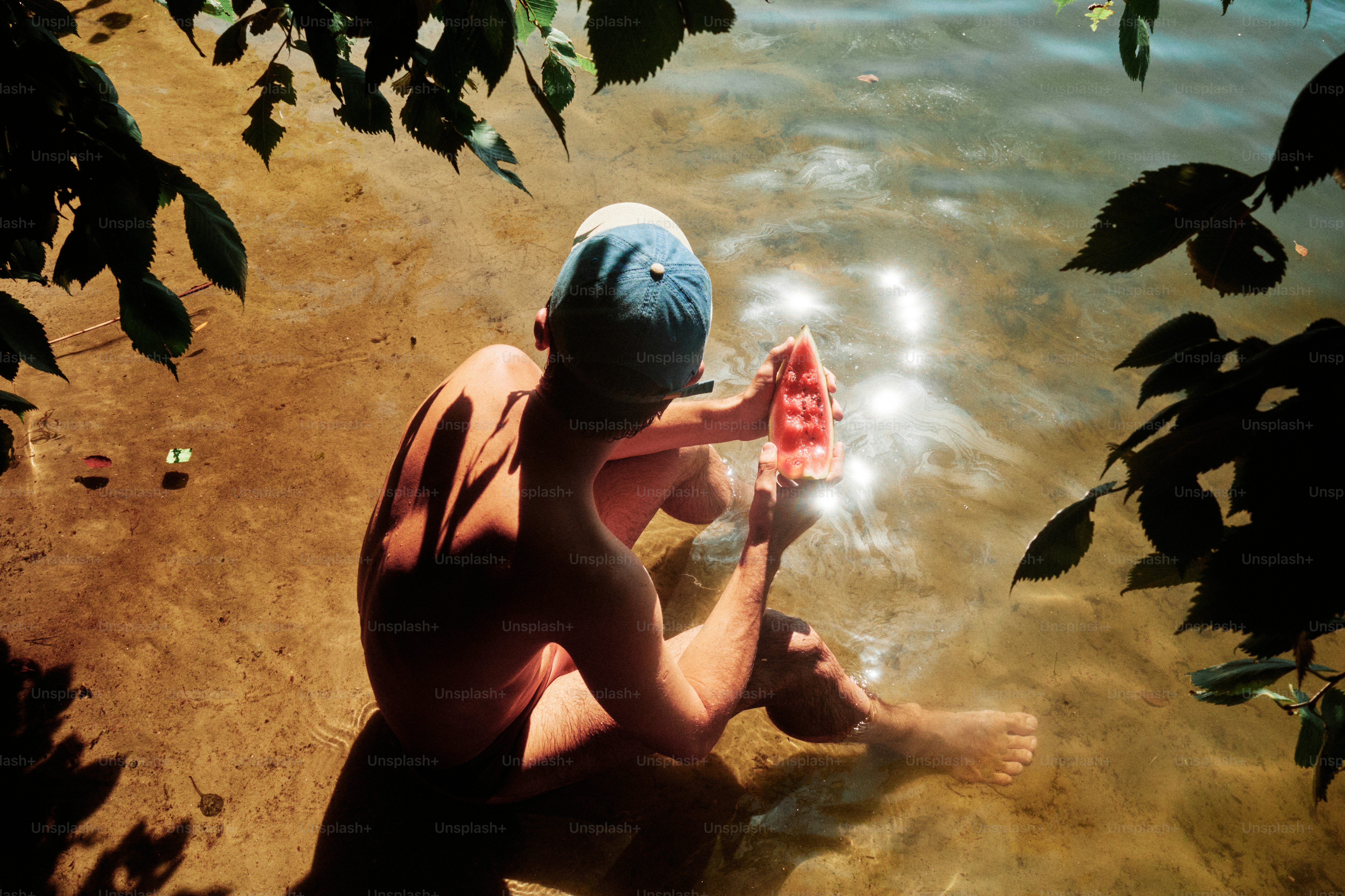 A person sits in the water, eating watermelon.