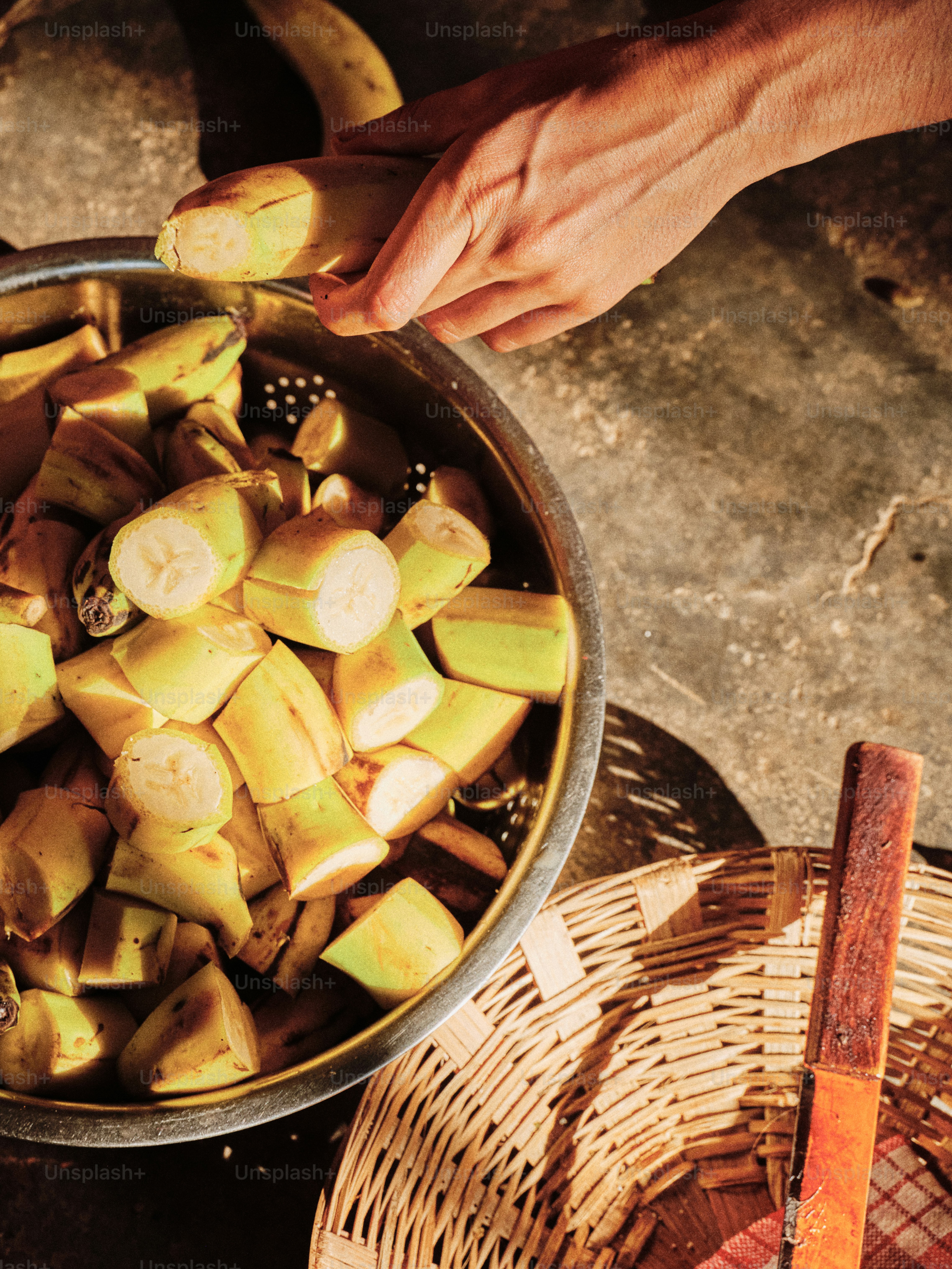A hand slices bananas into a colander.